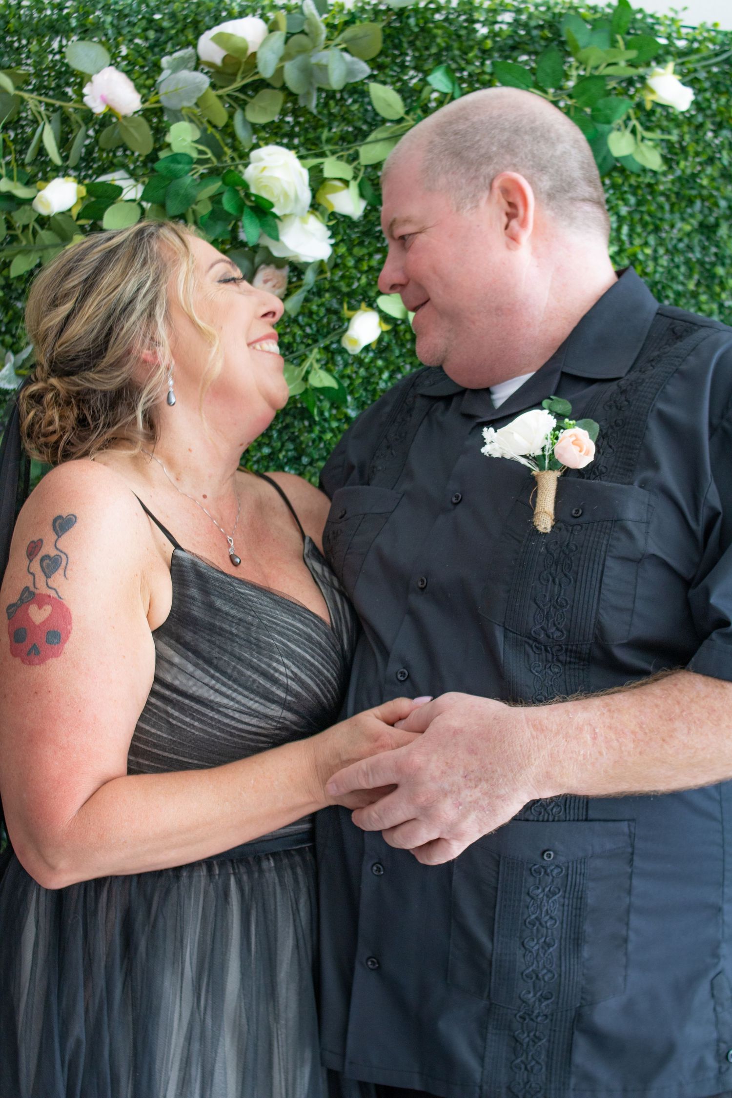 Candid laughing moment captured against floral wall backdrop at celebration.