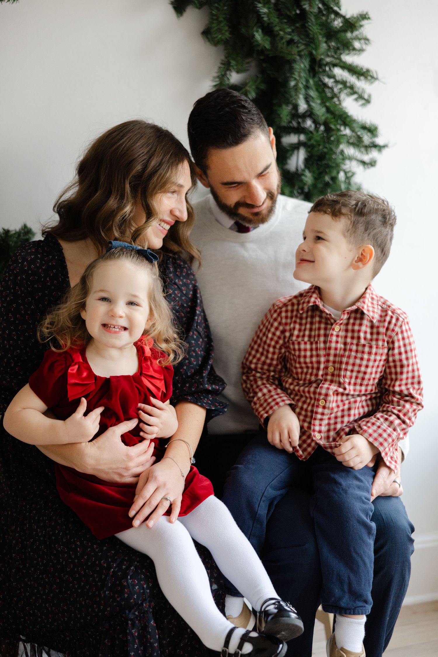 A family shares joyful laughter together while sitting against a wall with evergreen holiday decor.