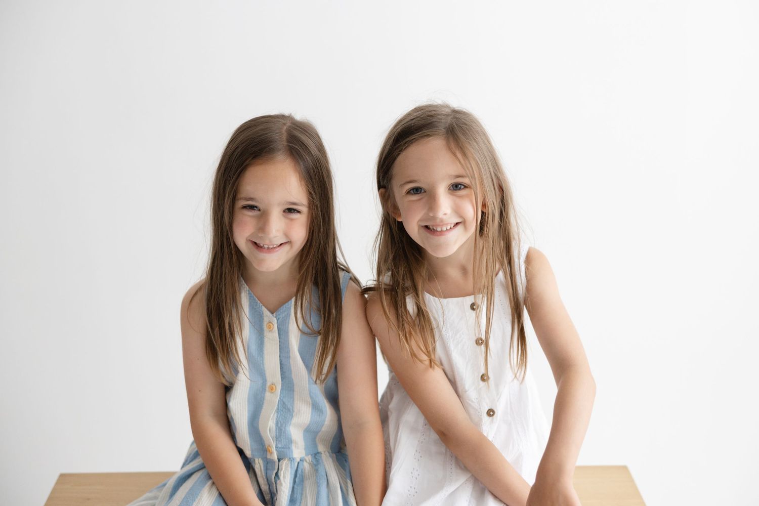 Two young girls in matching blue and white striped dresses pose together with bright happy smiles.