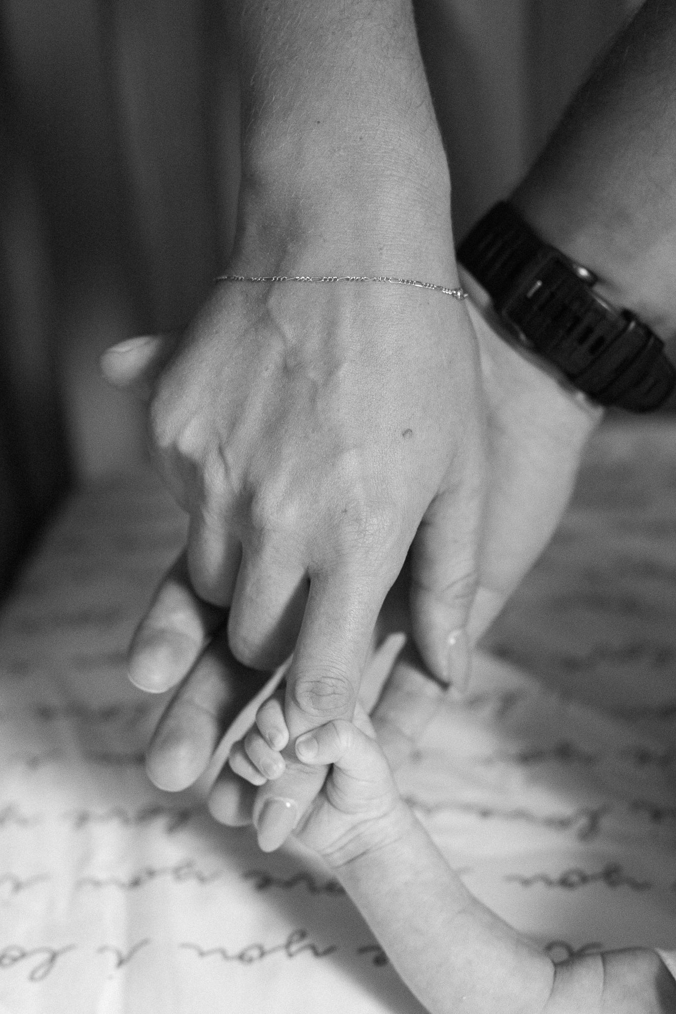 black and white photo of new parents holding hand of newborn