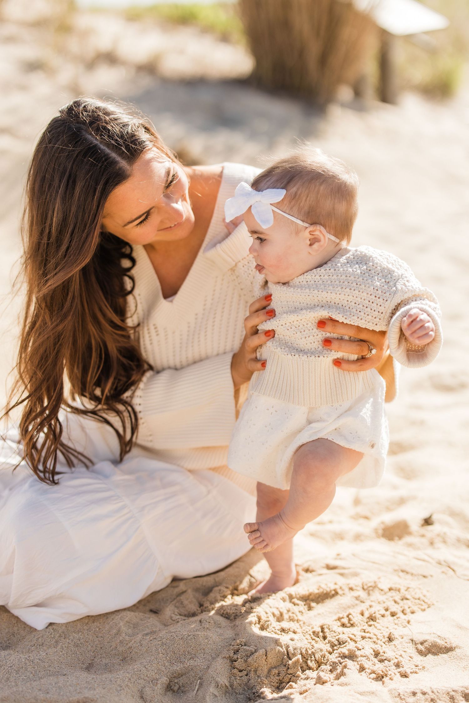 mom and daughter sitting on sand at the beach