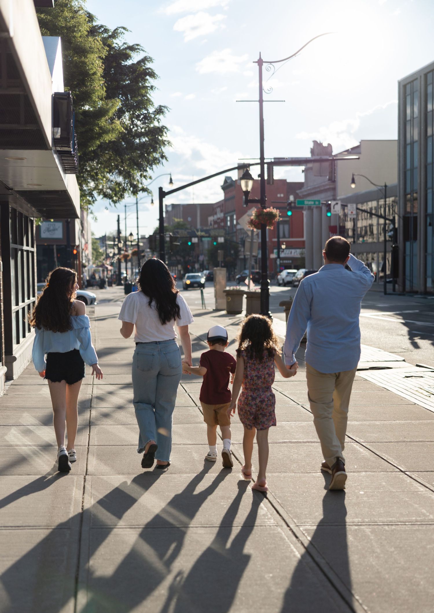 Group of people walking together casting long shadows on a sunny sidewalk in an urban shopping district.