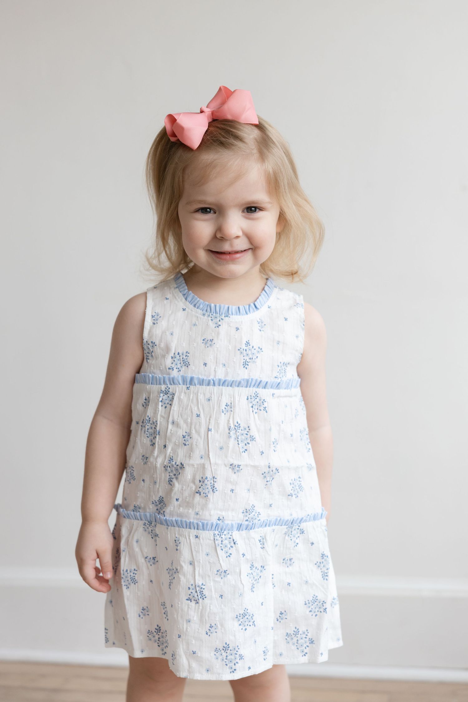 A child in a white and blue floral dress with a pink bow smiles in a progression of four similar poses.