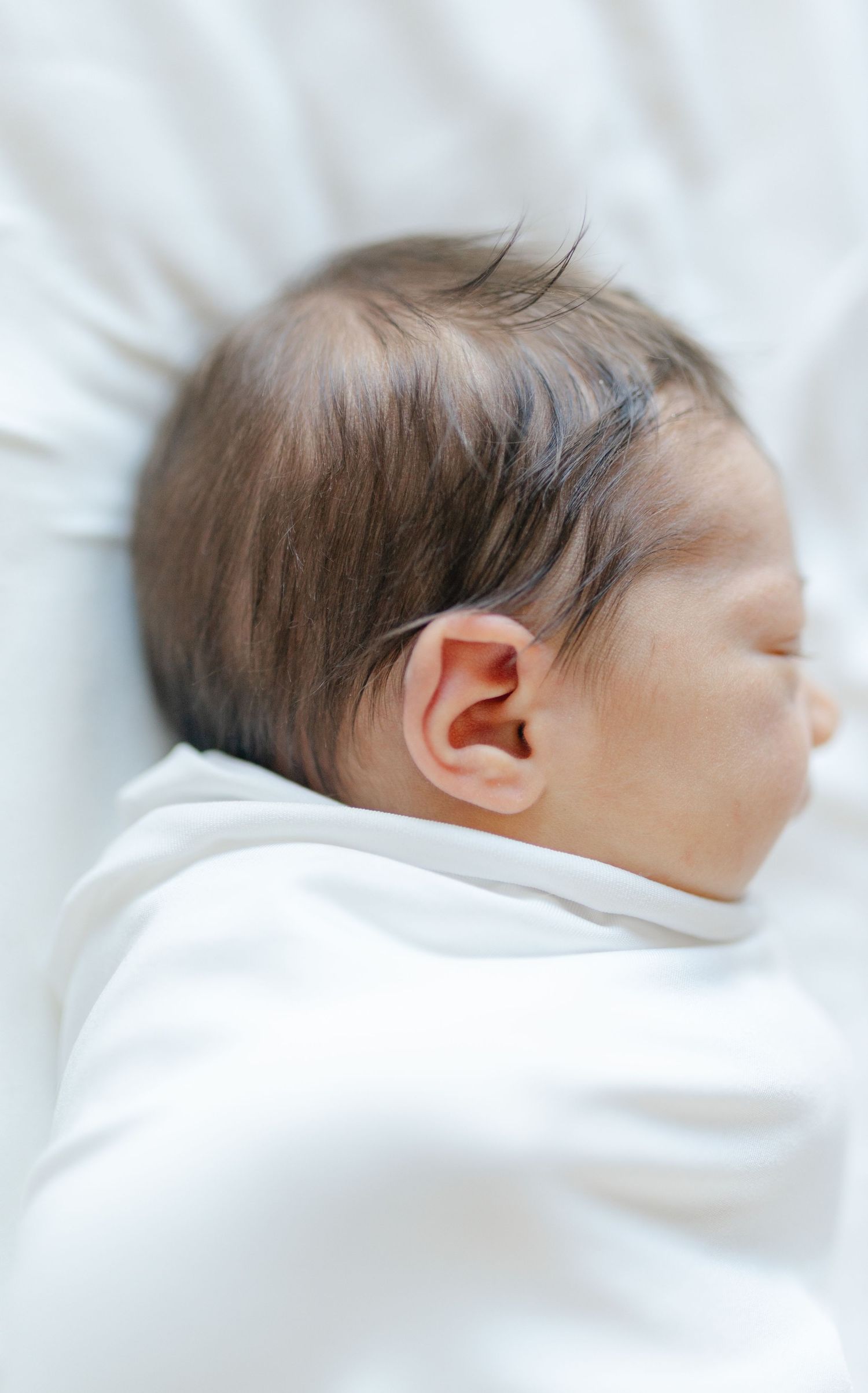 A sleeping baby wrapped in soft white blankets rests peacefully in a series of side-view photos.