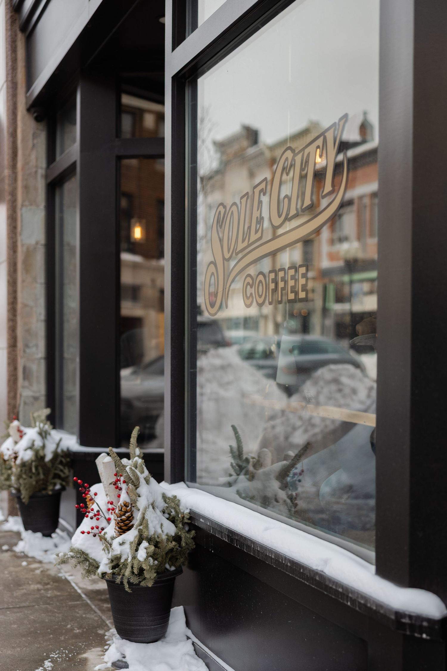 Snow accumulates on windowsills outside a storefront with vintage-style signage and winter floral arrangements.