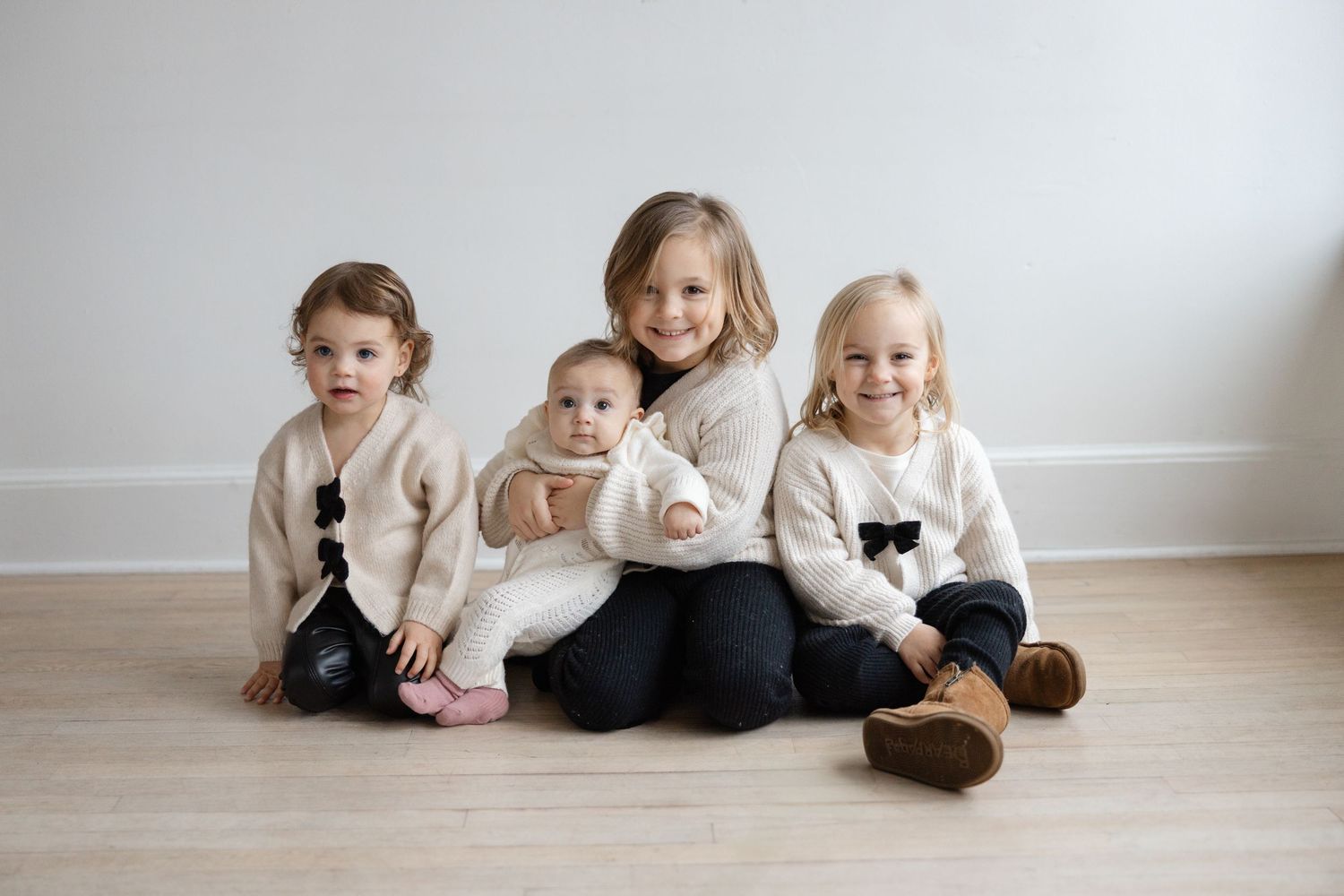 Children lying on a light wooden floor in matching black and white outfits creating a sweet family portrait.