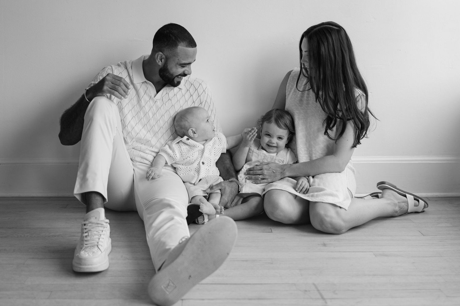 A family sits together on a hardwood floor in a black and white photograph.