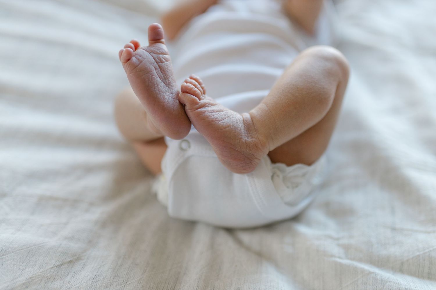 Close-up view of tiny baby feet and legs in white clothing resting on white bedding.