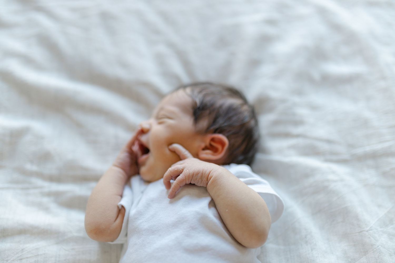 A sleeping baby lies on white bedding with arms raised above their head in a peaceful pose.