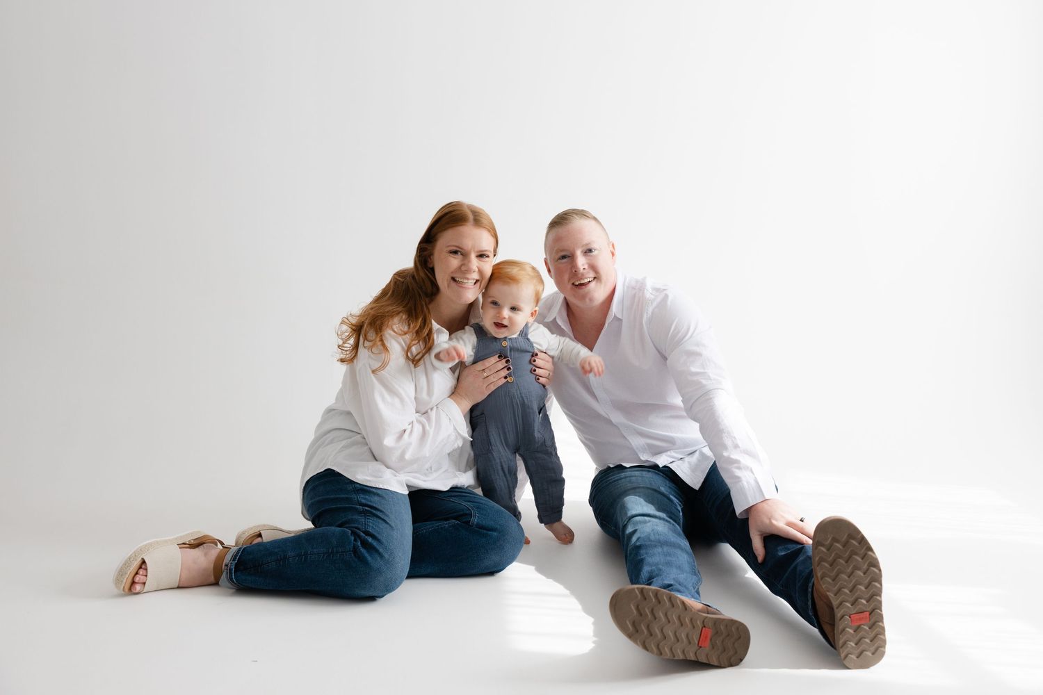 A couple in white shirts and jeans lies on a white floor in a series of playful, candid poses.