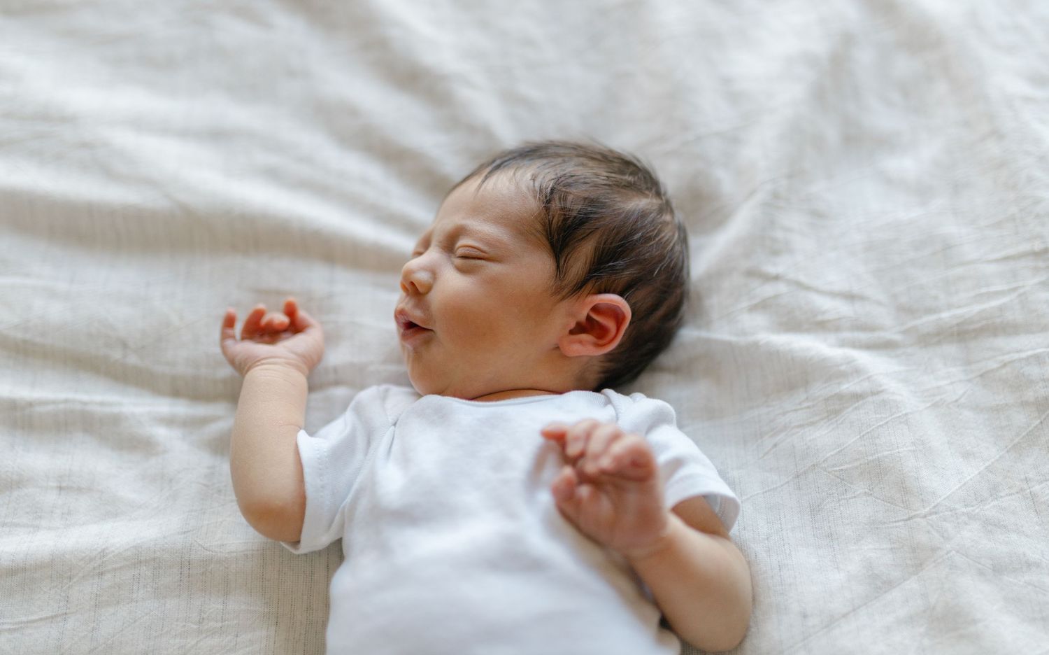 A sleeping baby in white clothing lies peacefully on white bedding in a series of connected photos.