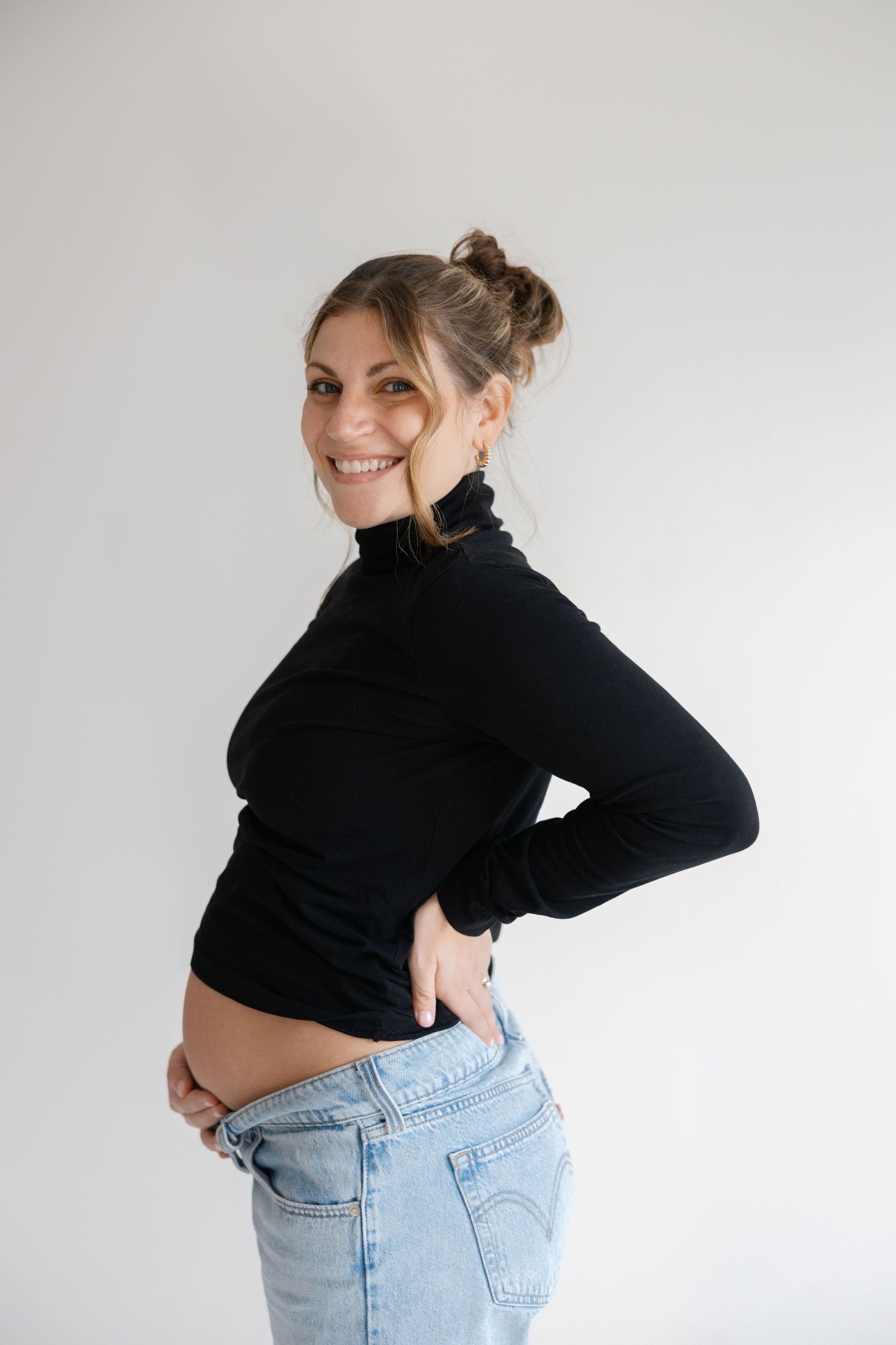 Woman in black turtleneck crop top and light wash jeans poses against white background in multiple angles.