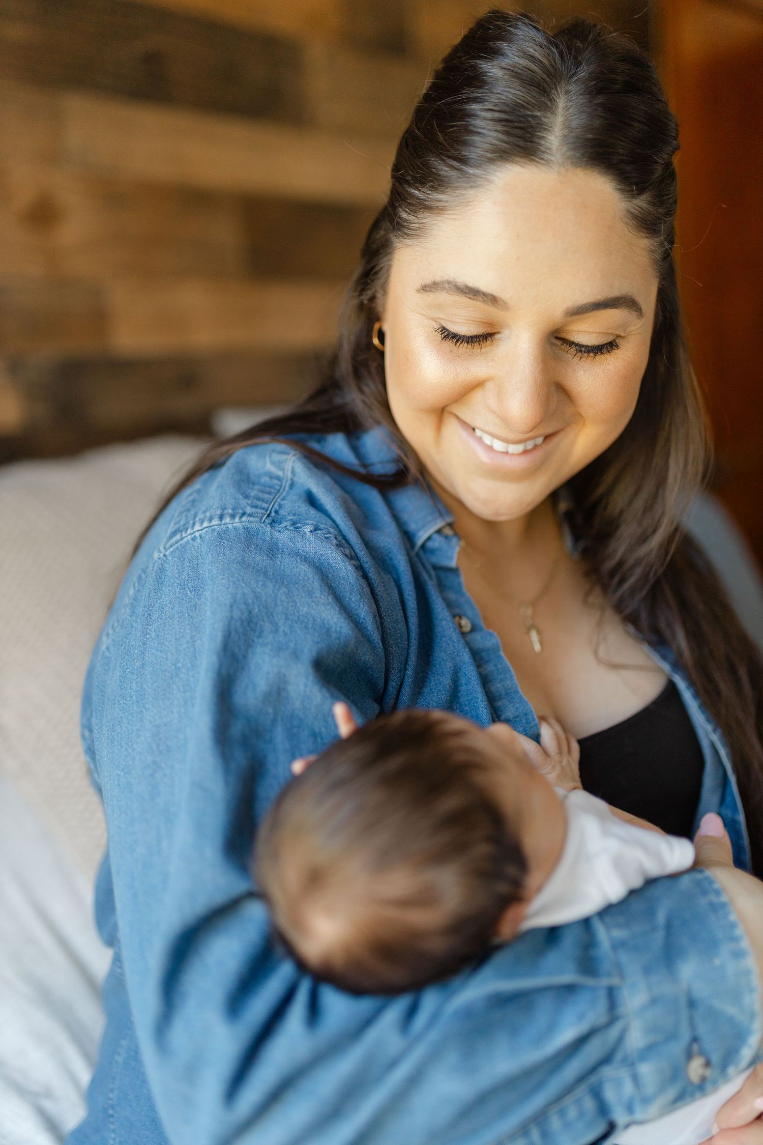 A tender moment between parent and infant in soft lighting, wearing a denim shirt against a warm background.