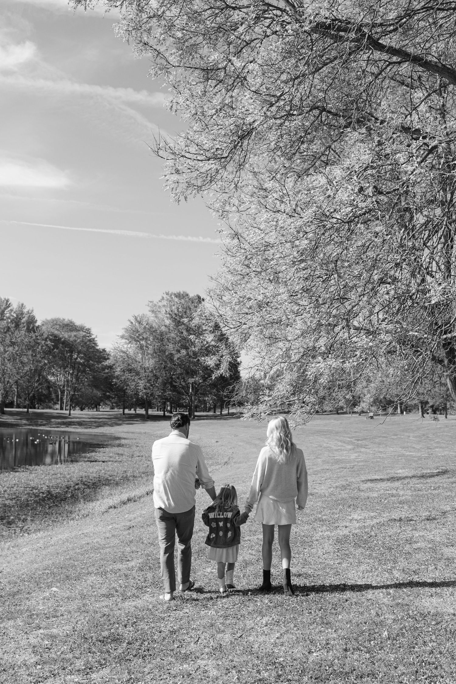 Three people walk together along a grassy hill lined with bare winter trees in black and white.