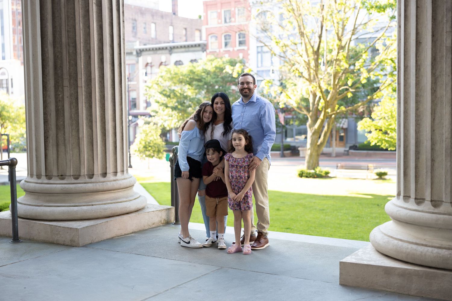 Group of people gather under classical stone columns at a university or government building on a sunny day.