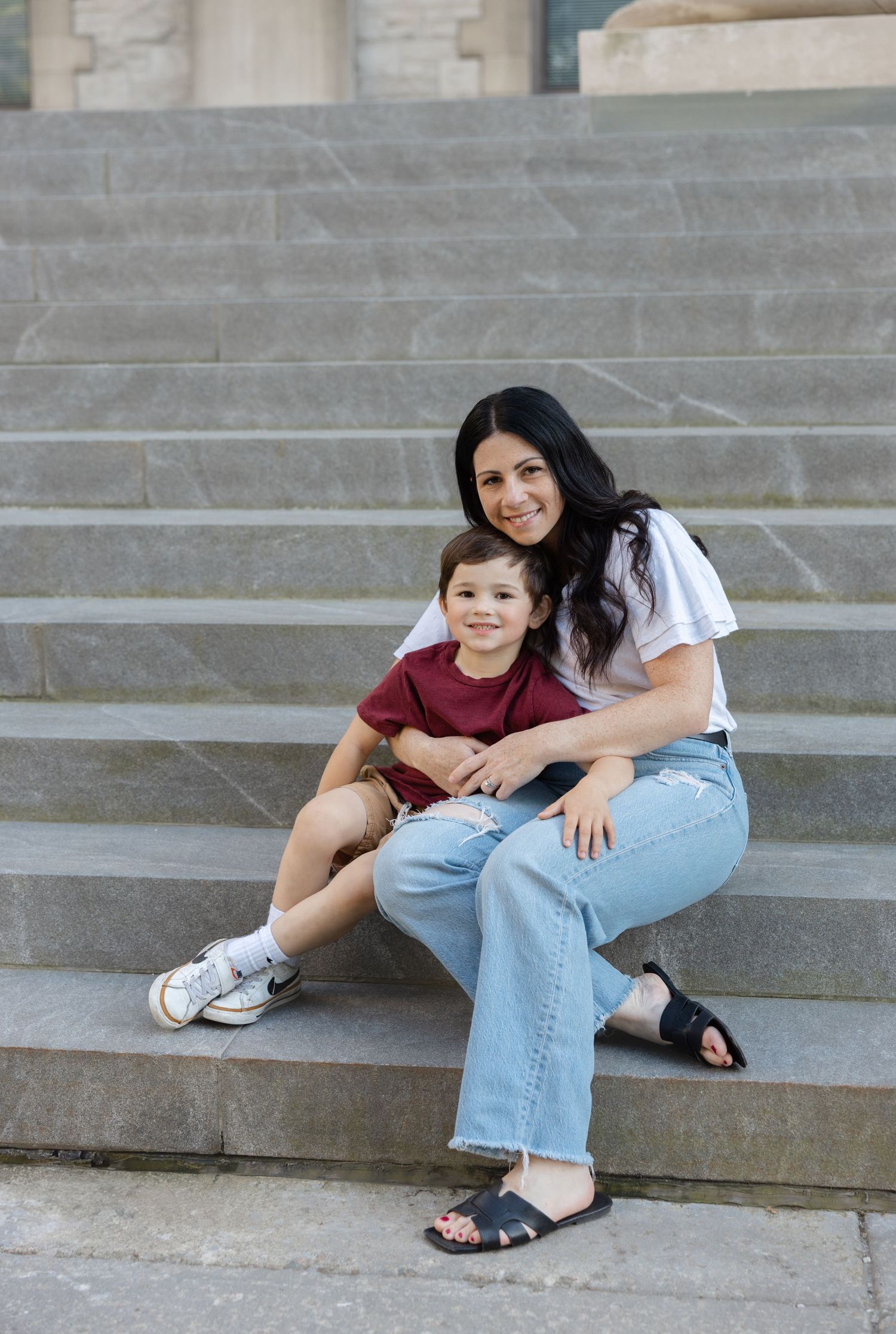 A casual moment captured on stone steps with parent and child sitting together in coordinating blue and burgundy outfits.