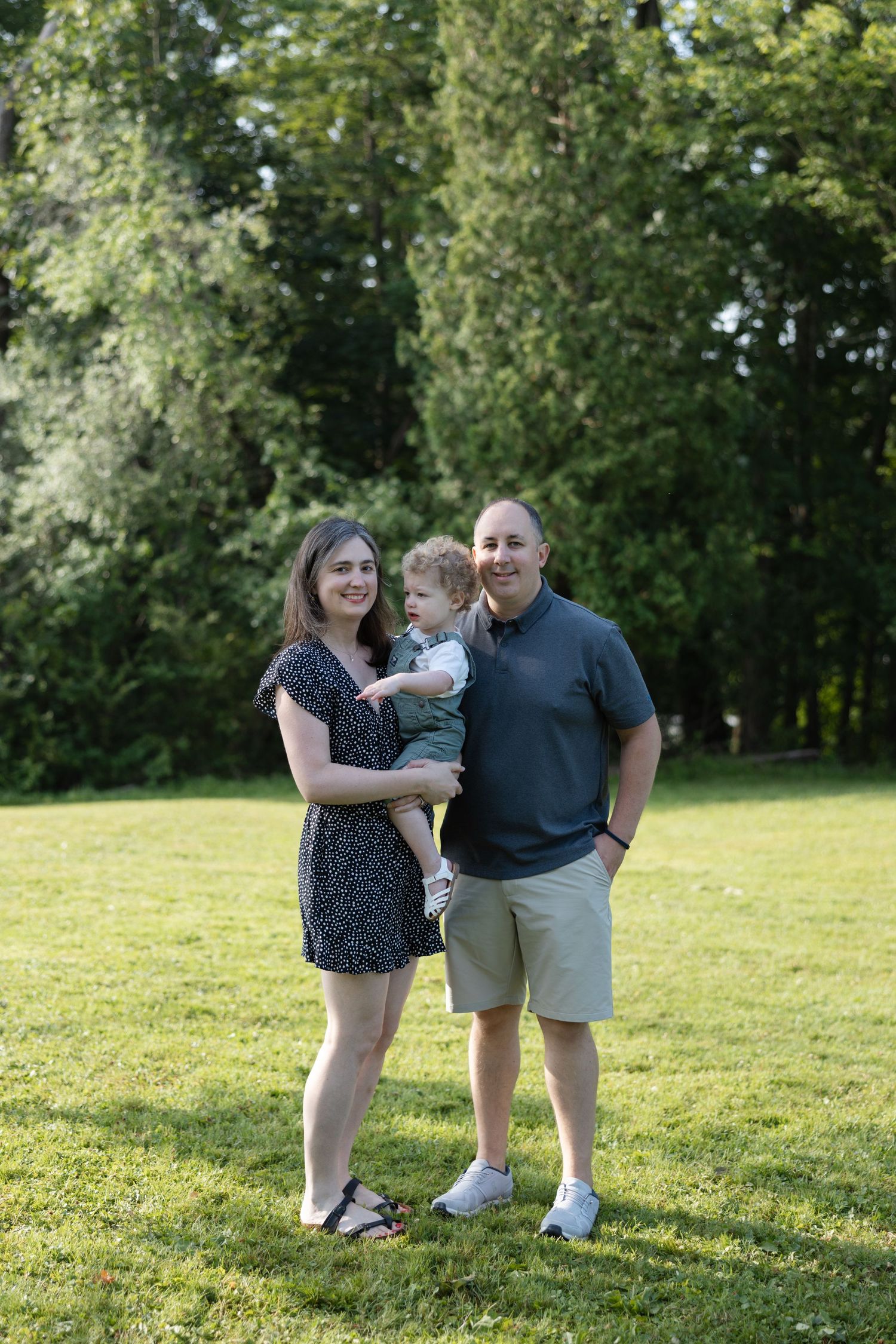A loving family plays together on a sunny day in a grassy park setting.