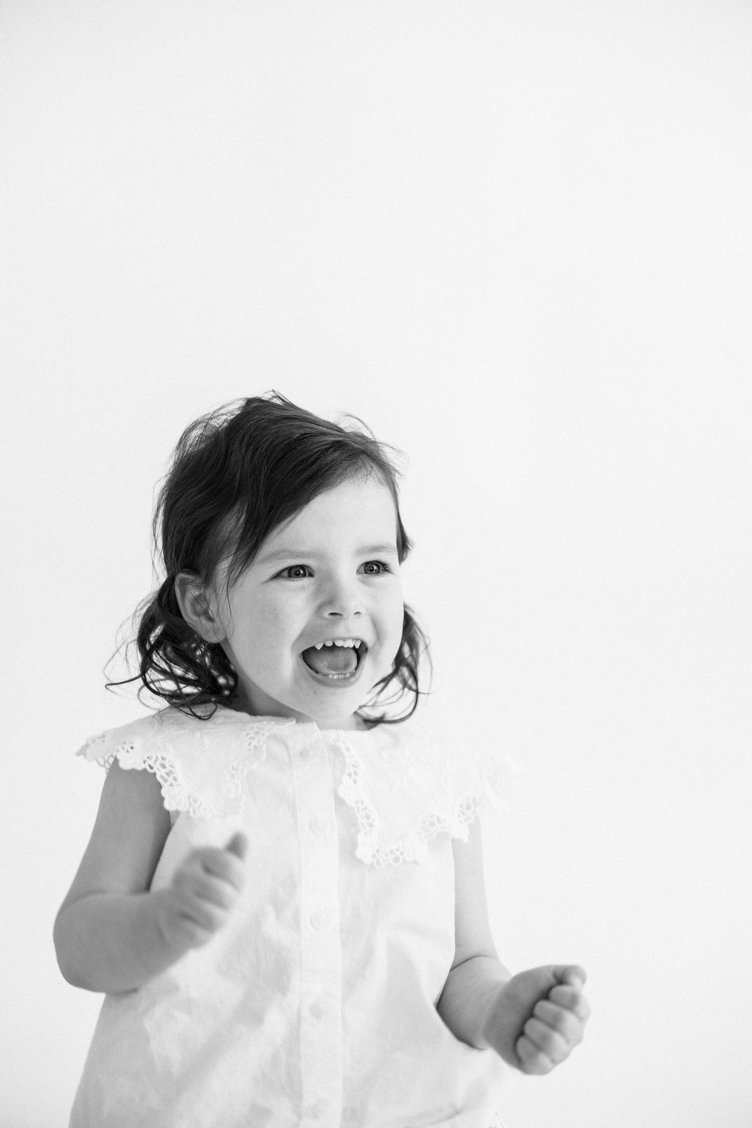 A series of black and white photos showing a joyful child in a white dress laughing and playing.
