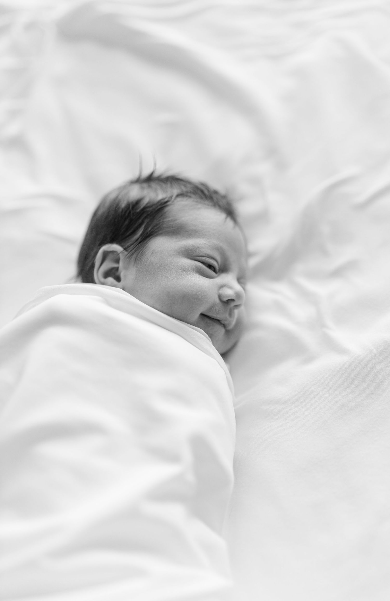 A sleeping baby wrapped in white blankets lies peacefully on white bedding.