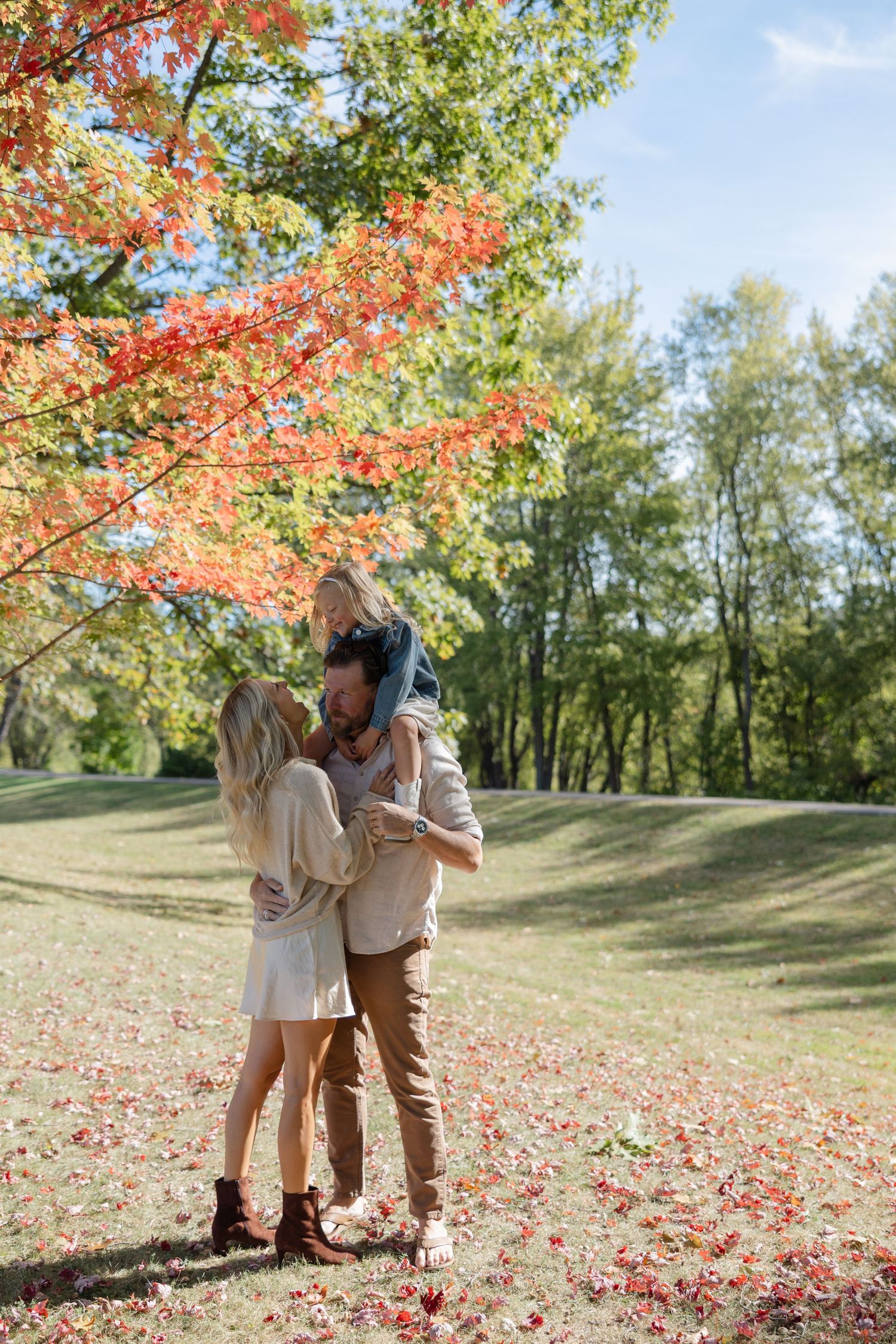 Tender autumn moment beneath vibrant red maple trees with fallen leaves scattered on grassy hillside.