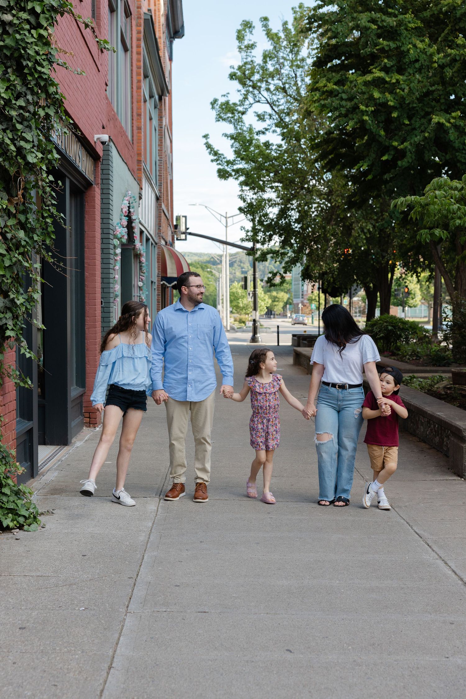 Four candid outdoor photos of family members walking together on a city sidewalk lined with brick buildings and trees.