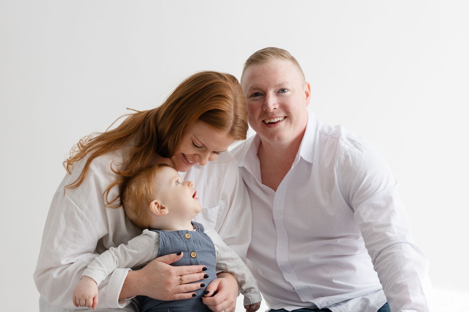 A couple in white shirts shares tender moments together while sitting on a light background.