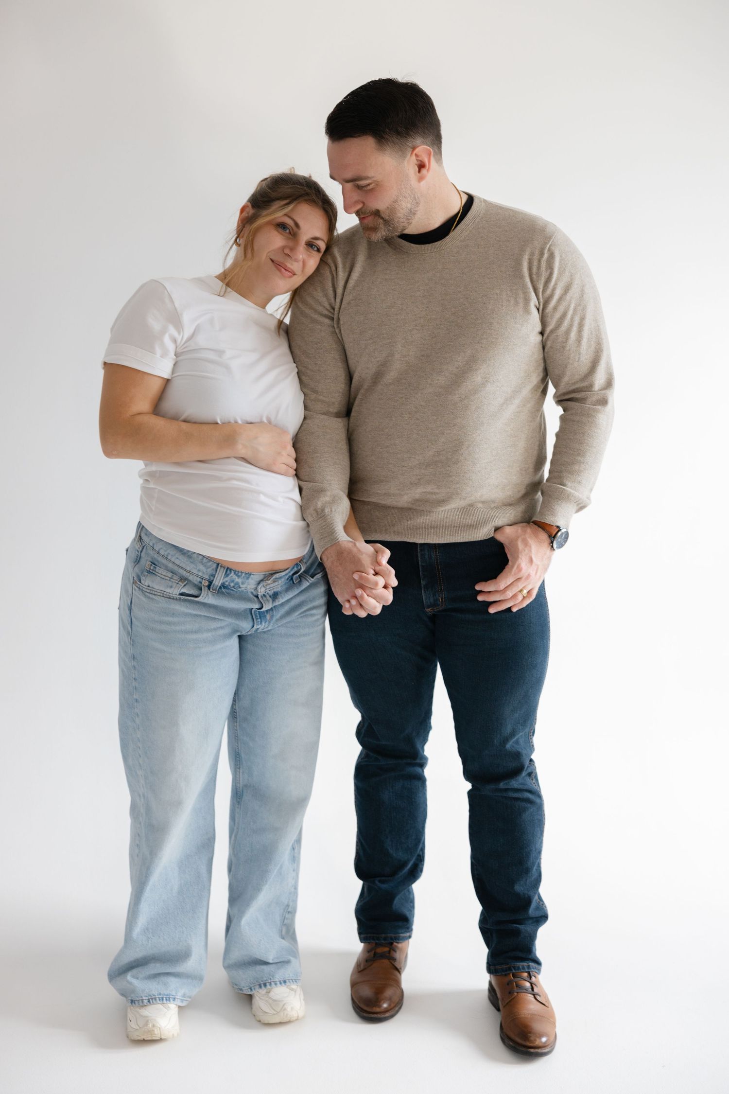 A couple in casual attire poses together against a white backdrop in a minimalist photoshoot series.
