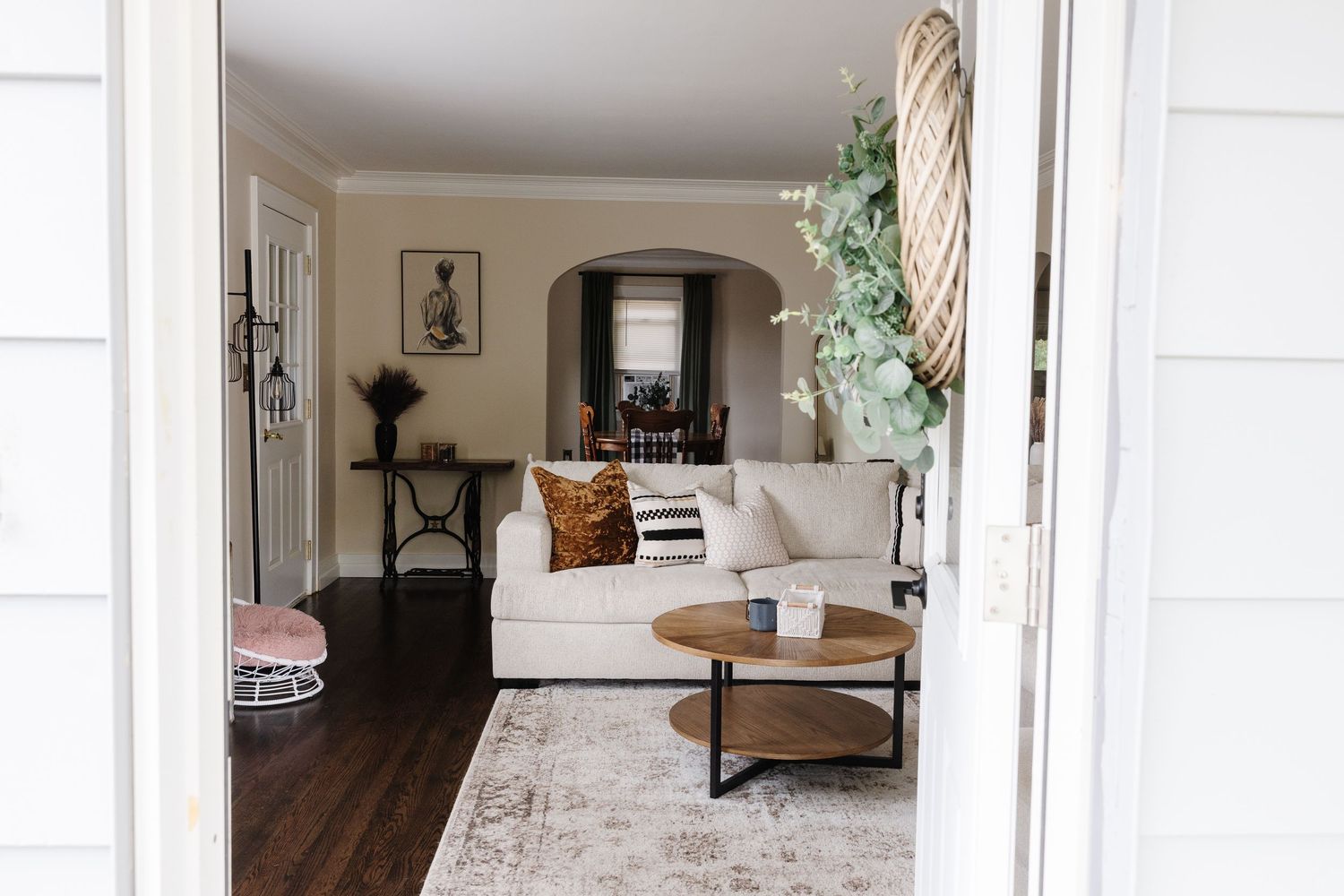 Modern living room with white sofa, round coffee table, and hardwood floors viewed through doorway entrance.
