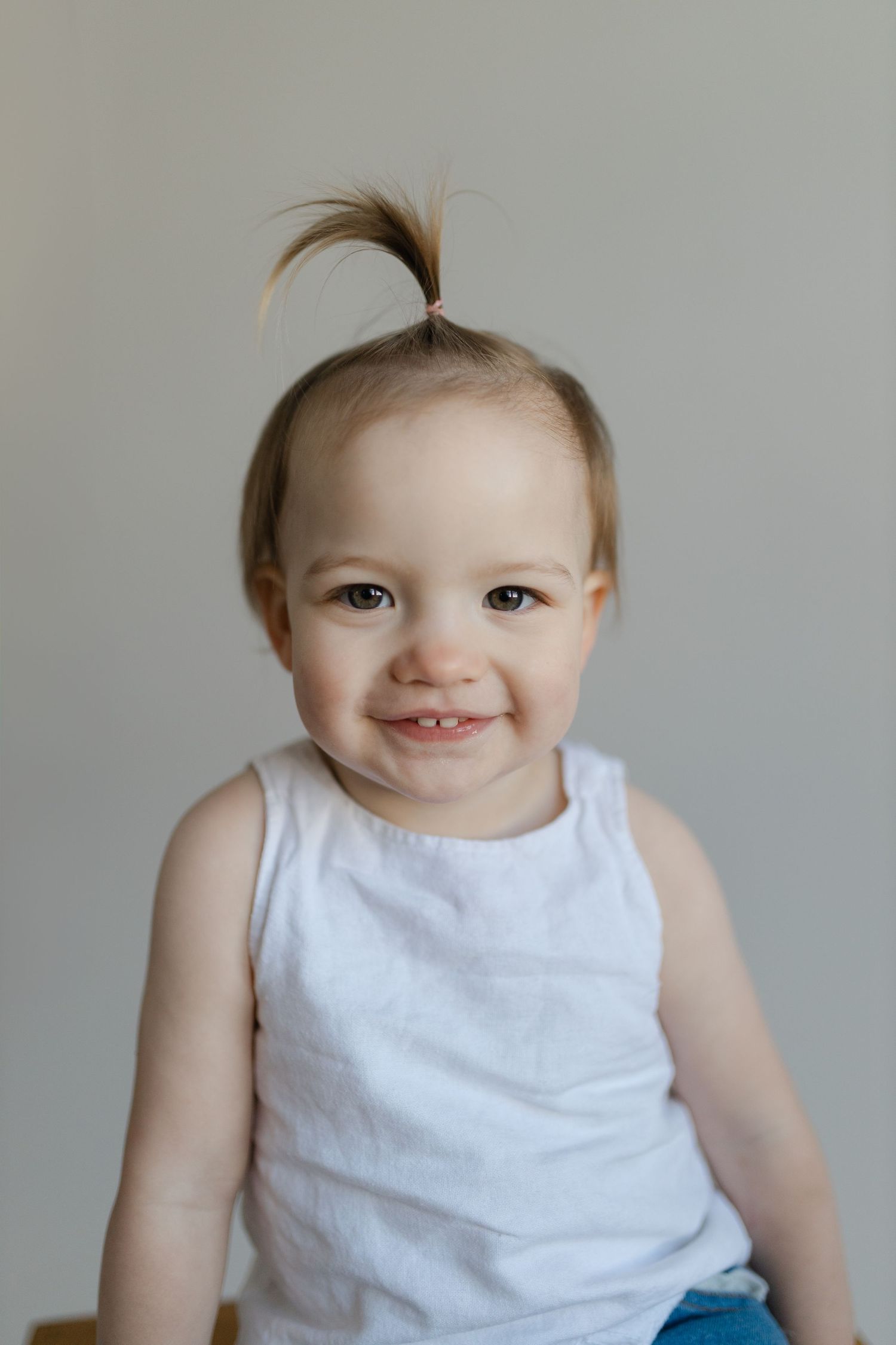 A collage of baby expressions showing joyful smiles while wearing a white sleeveless outfit against a gray background.