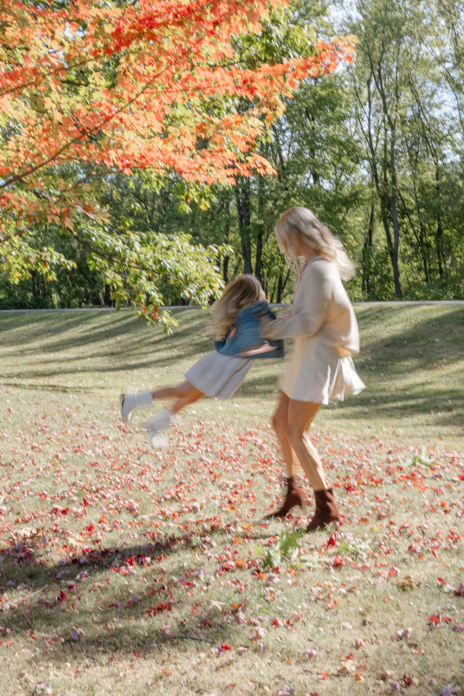 Playful scene in autumn with falling red maple leaves as figures enjoy a carefree moment under colorful foliage.