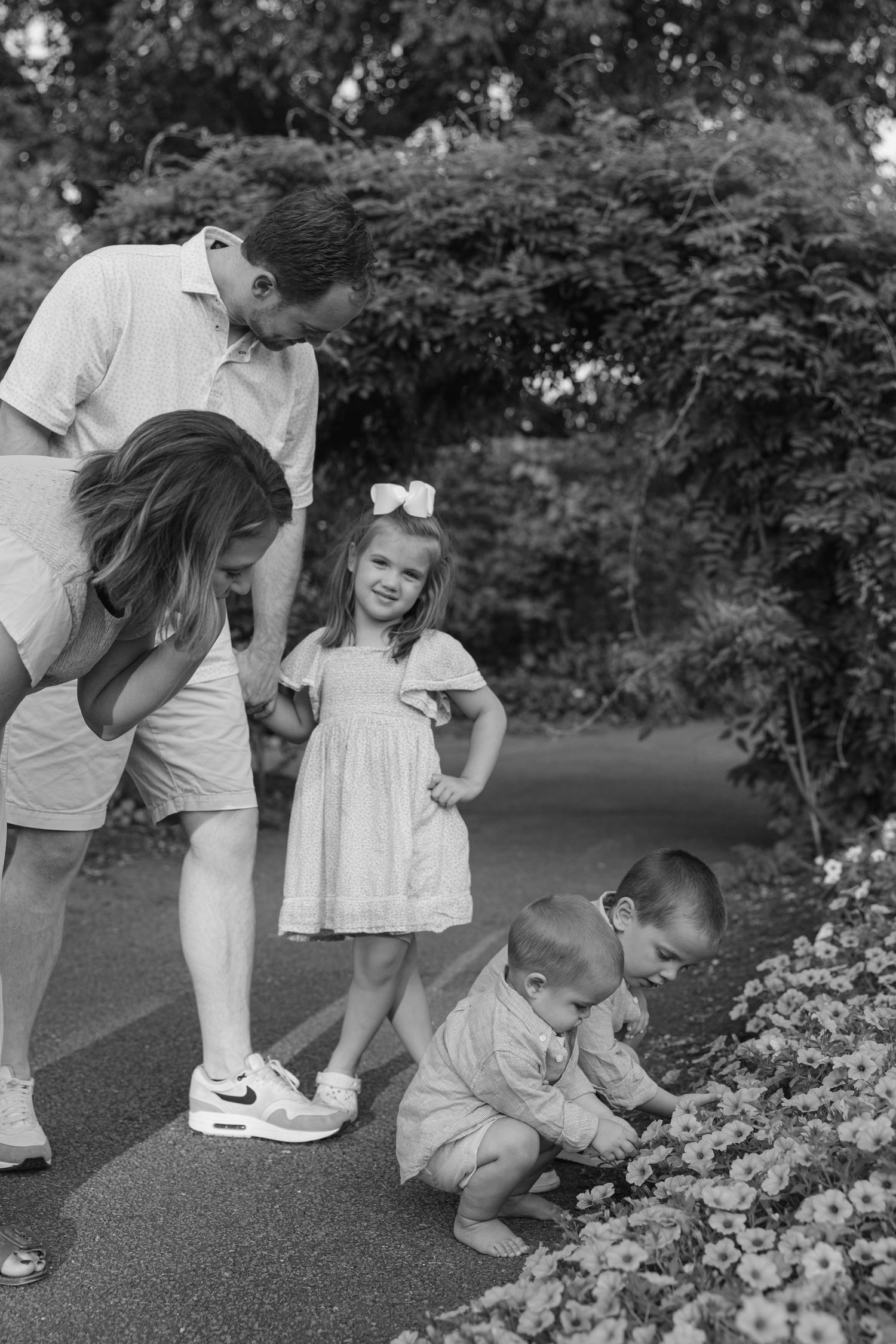 Family exploring and looking at flowers together in a lush garden setting on a sunny day.