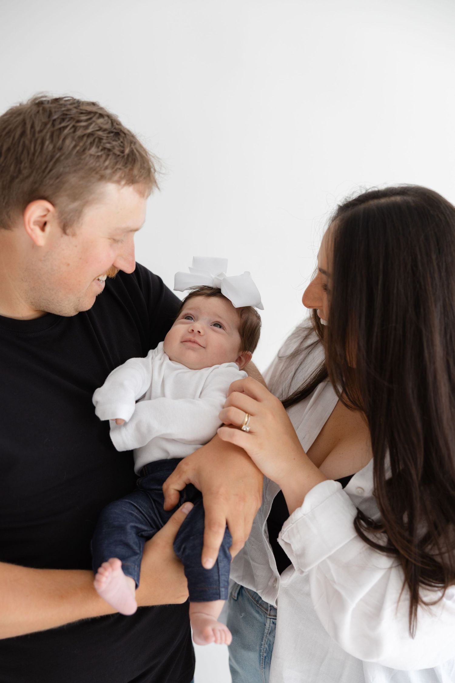 Parents adoringly hold their baby dressed in white during an intimate family portrait session.
