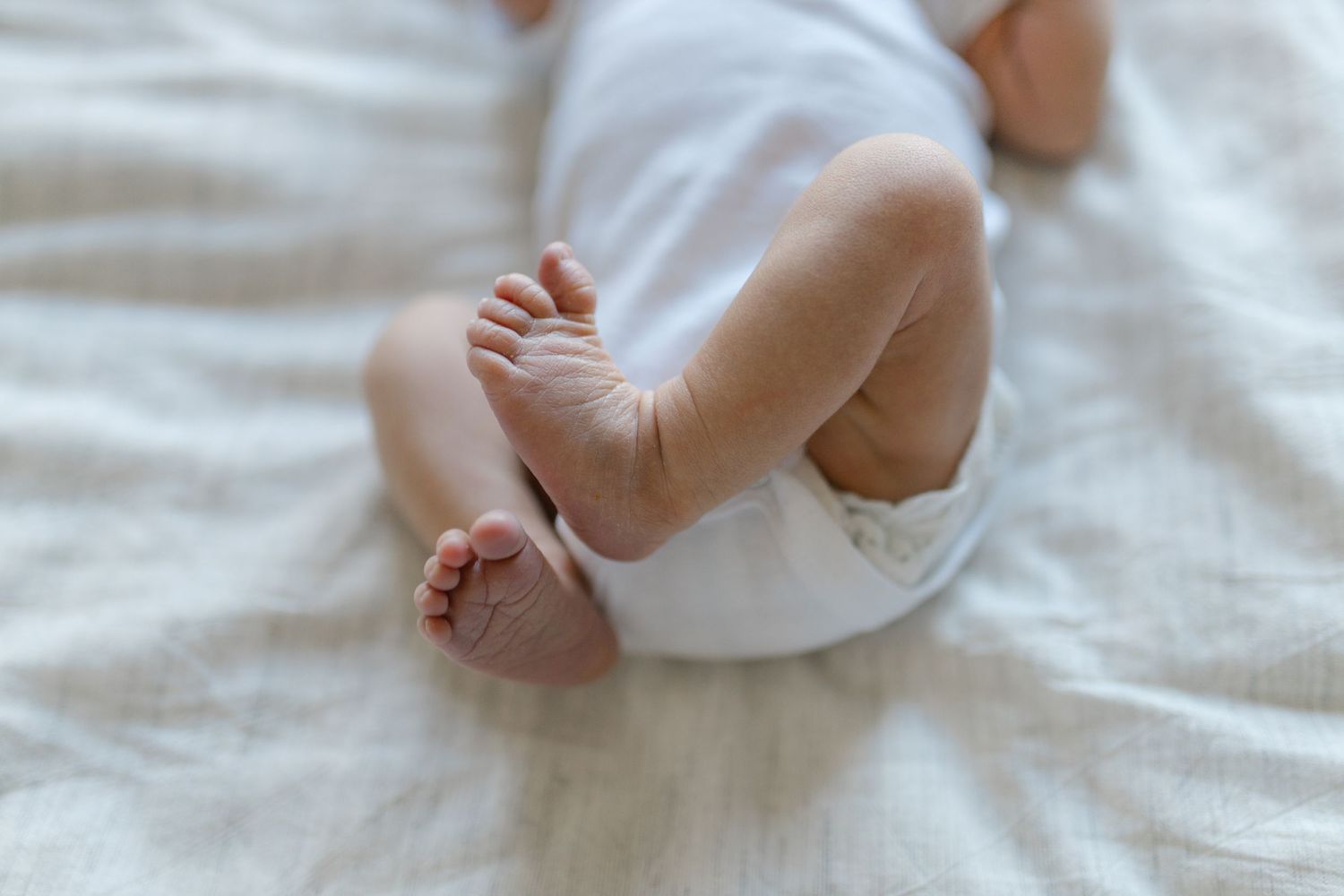Close-up view of tiny baby feet with wrinkled skin resting on soft white fabric.