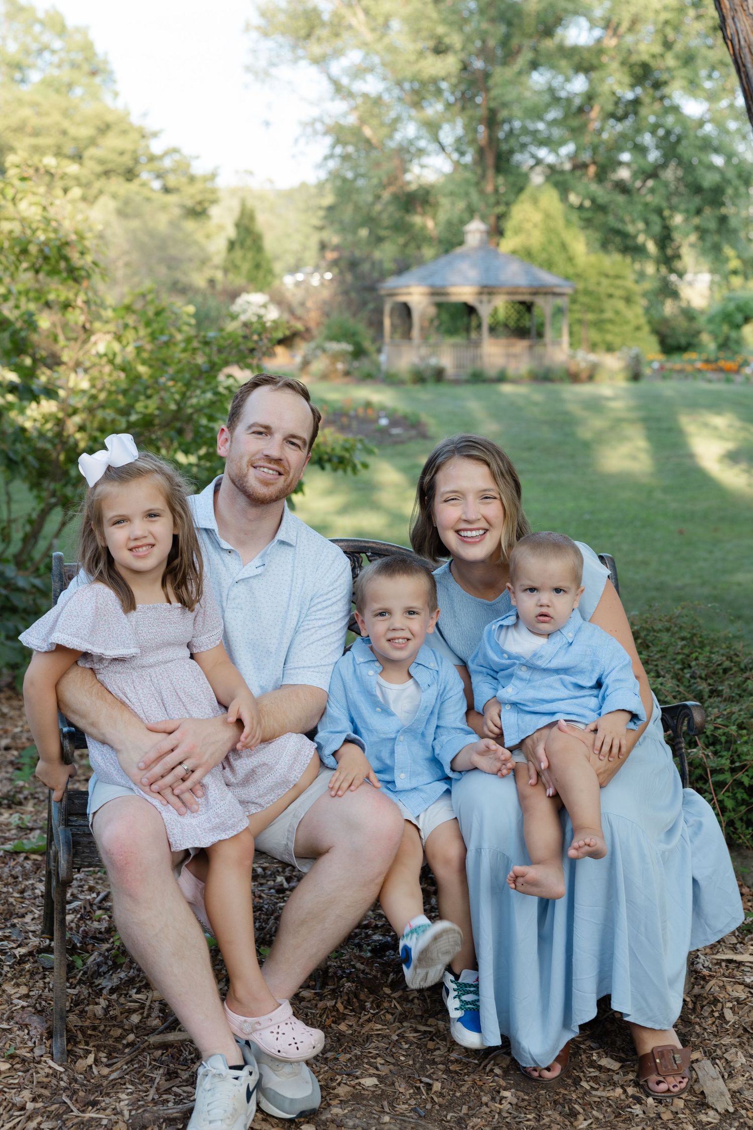 Family sitting together outdoors on a grassy hill with trees in the background wearing coordinated blue outfits.