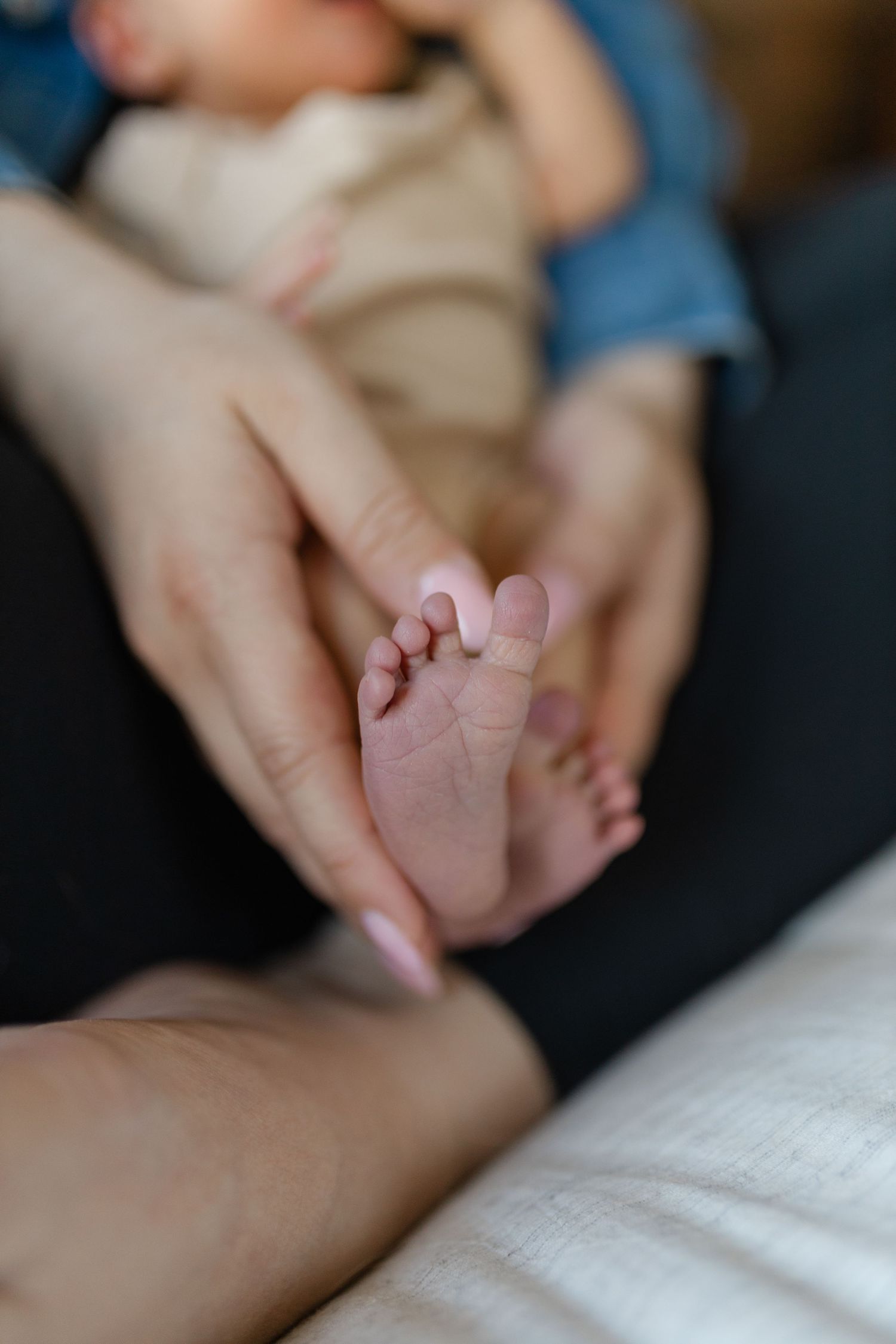 Close-up view of tiny newborn baby feet being gently held by caring hands against white bedding in soft lighting.