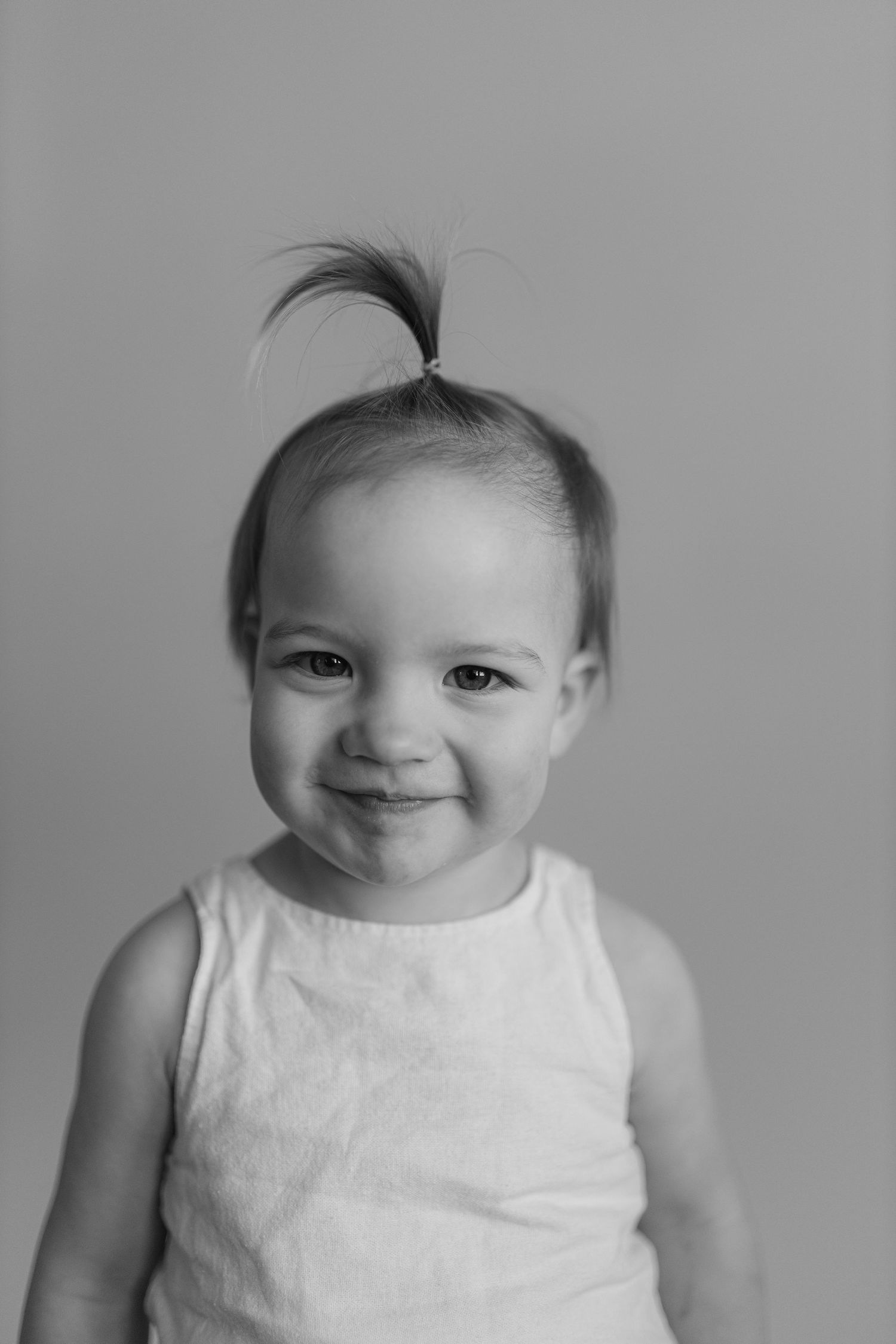 Black and white photo series showing a baby in a white sleeveless outfit making various playful expressions.