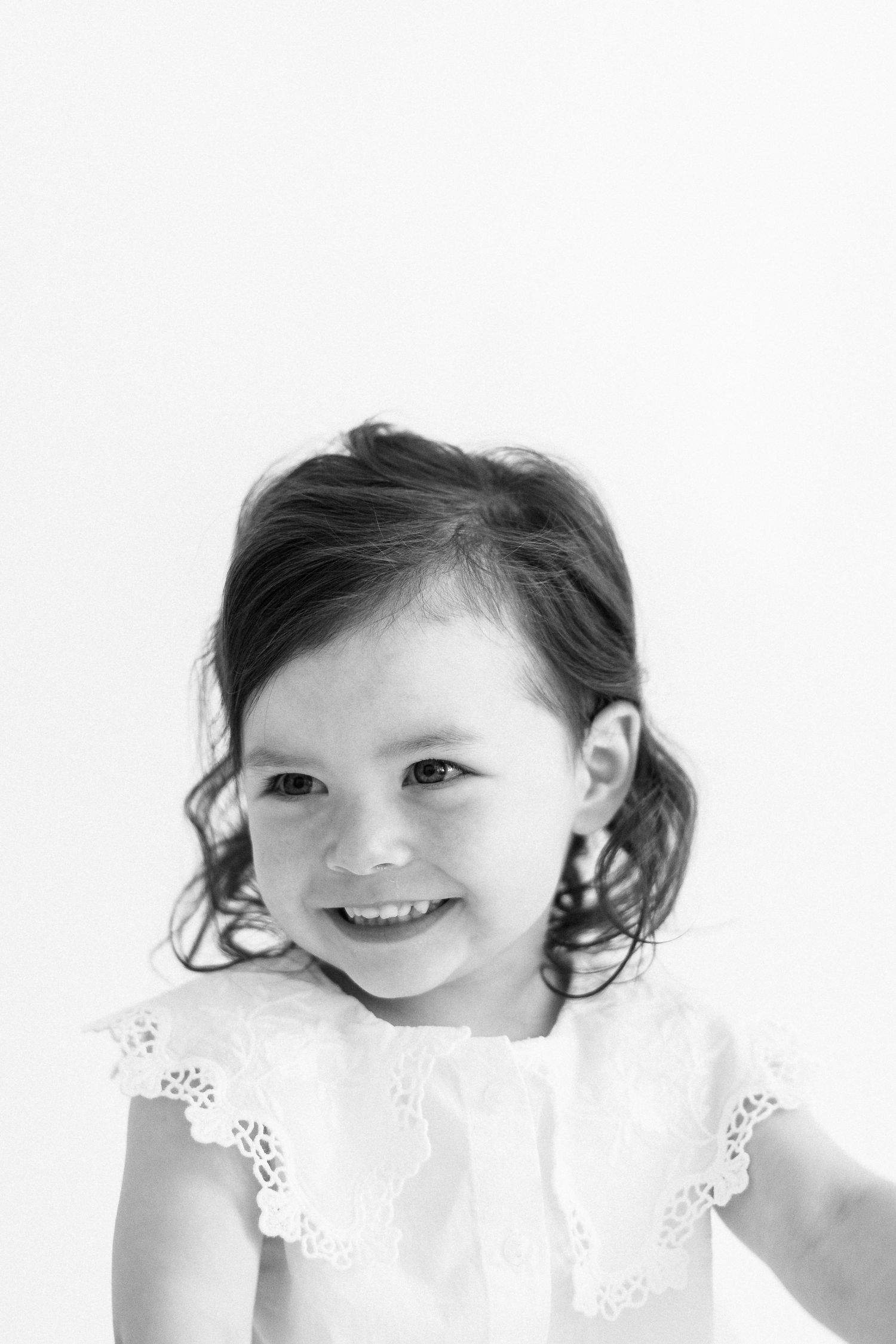 Three black and white portraits of a young child peeking playfully over a white lace handkerchief.