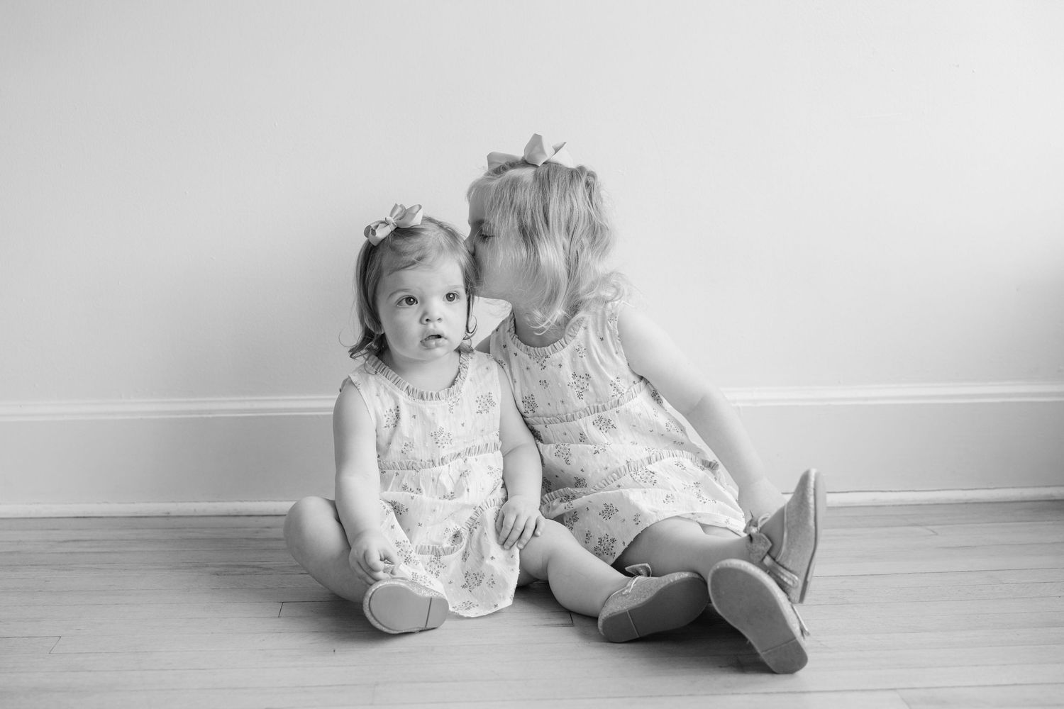 Black and white collage of toddlers sitting and playing together on hardwood floor.