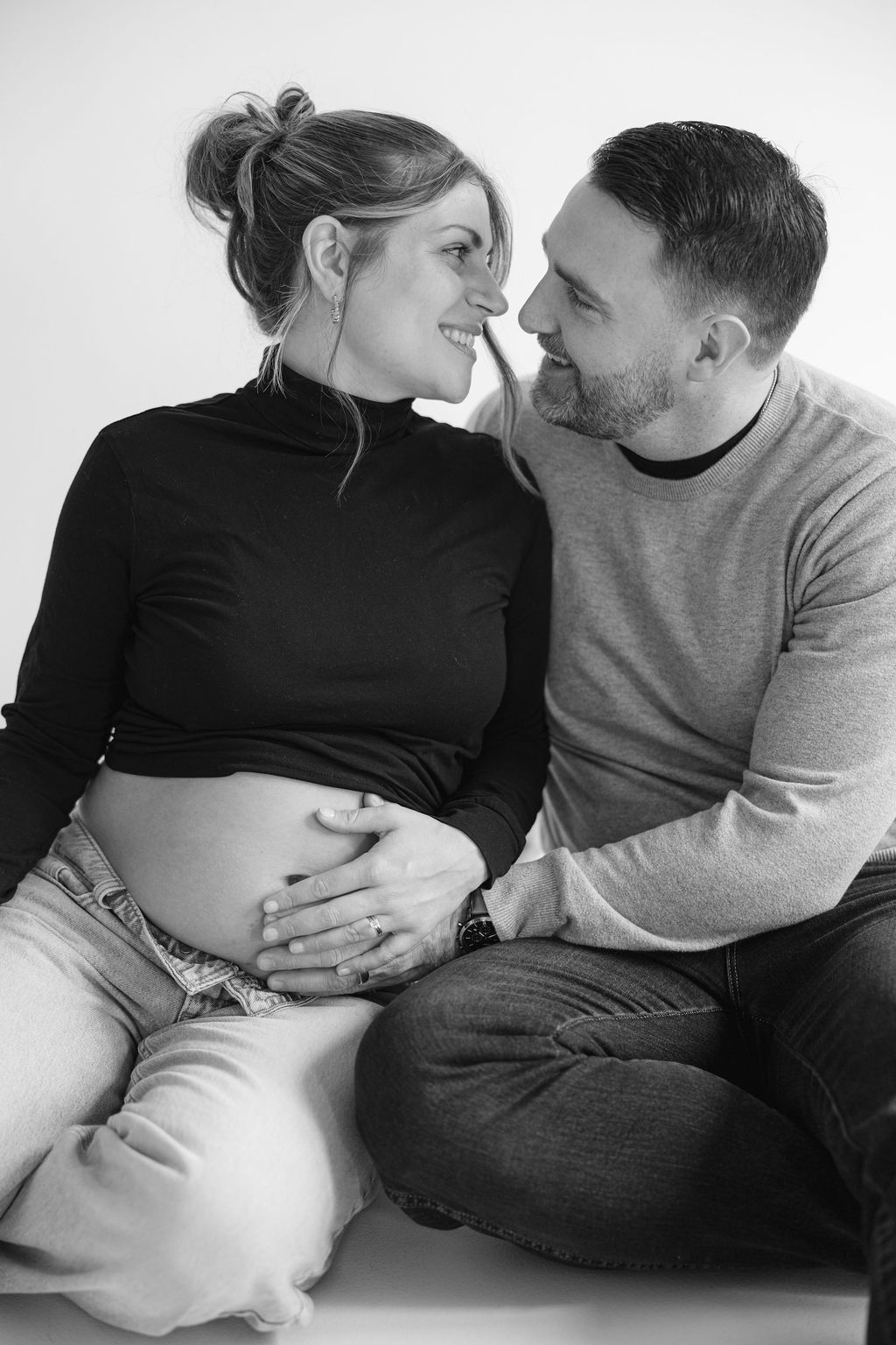A couple shares an intimate black and white maternity moment as they lovingly embrace the pregnant belly.
