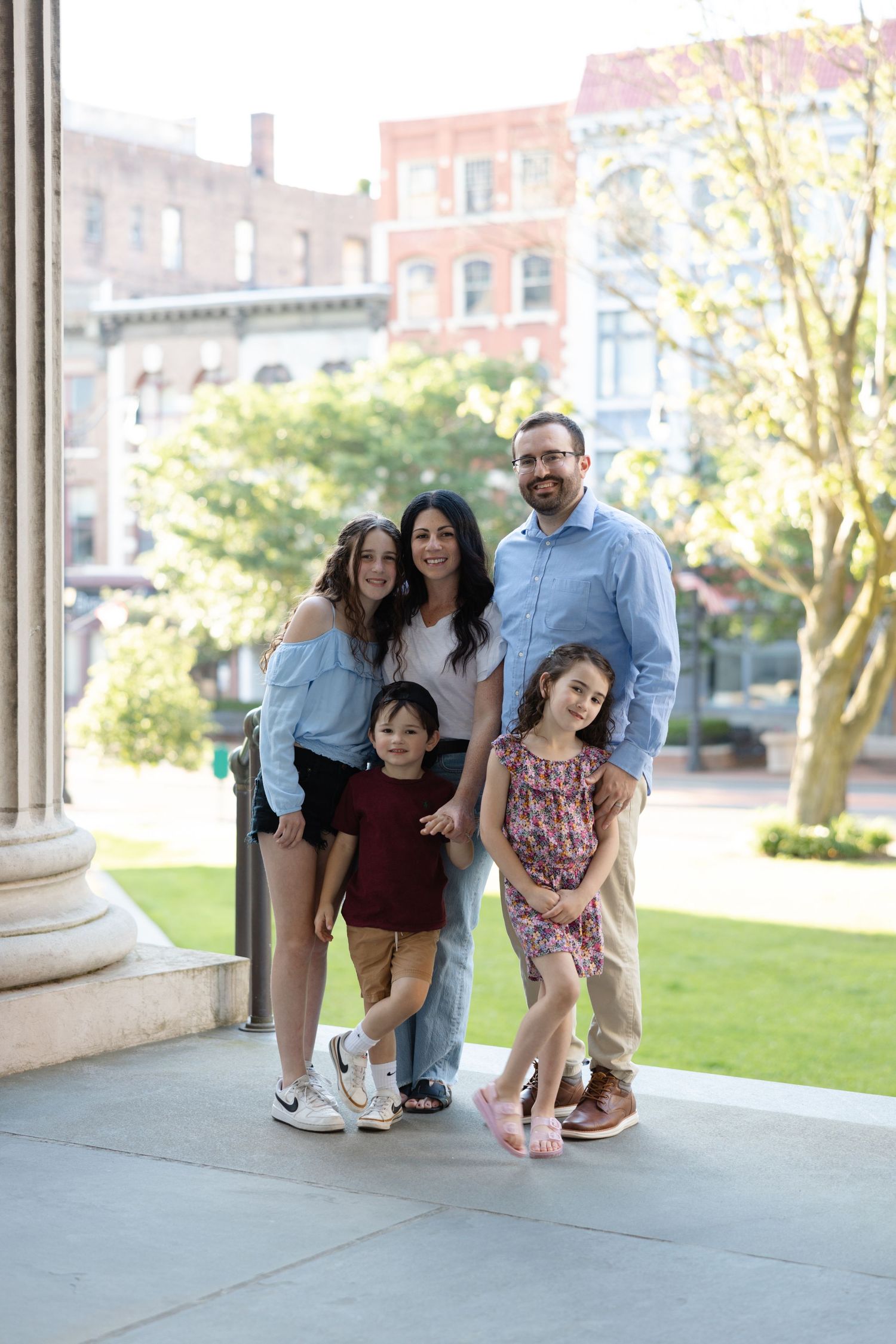 A family poses together in a series of candid shots on a porch with columns and greenery in the background.