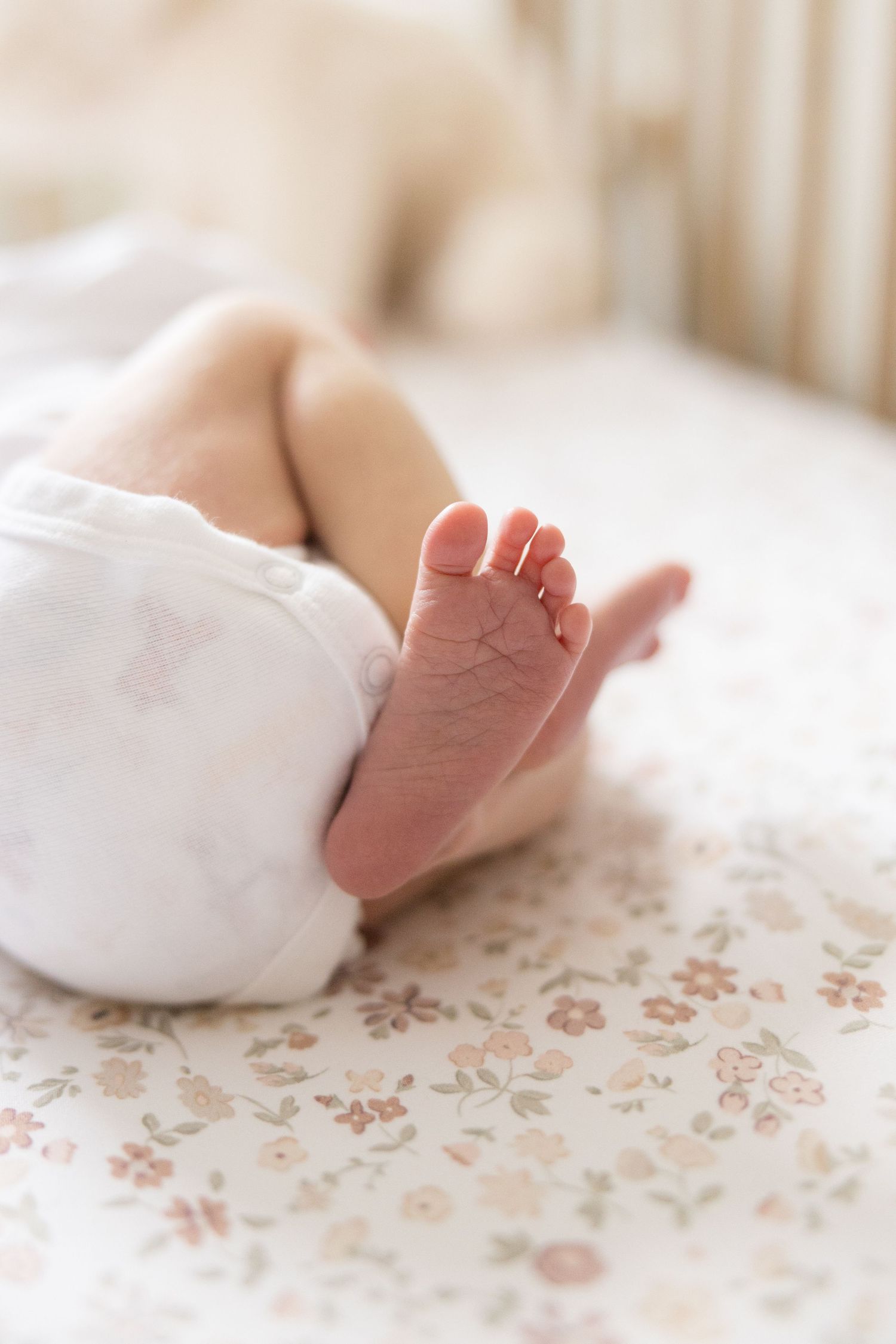 Close-up of tiny newborn baby foot resting on floral patterned bedding in soft natural light.