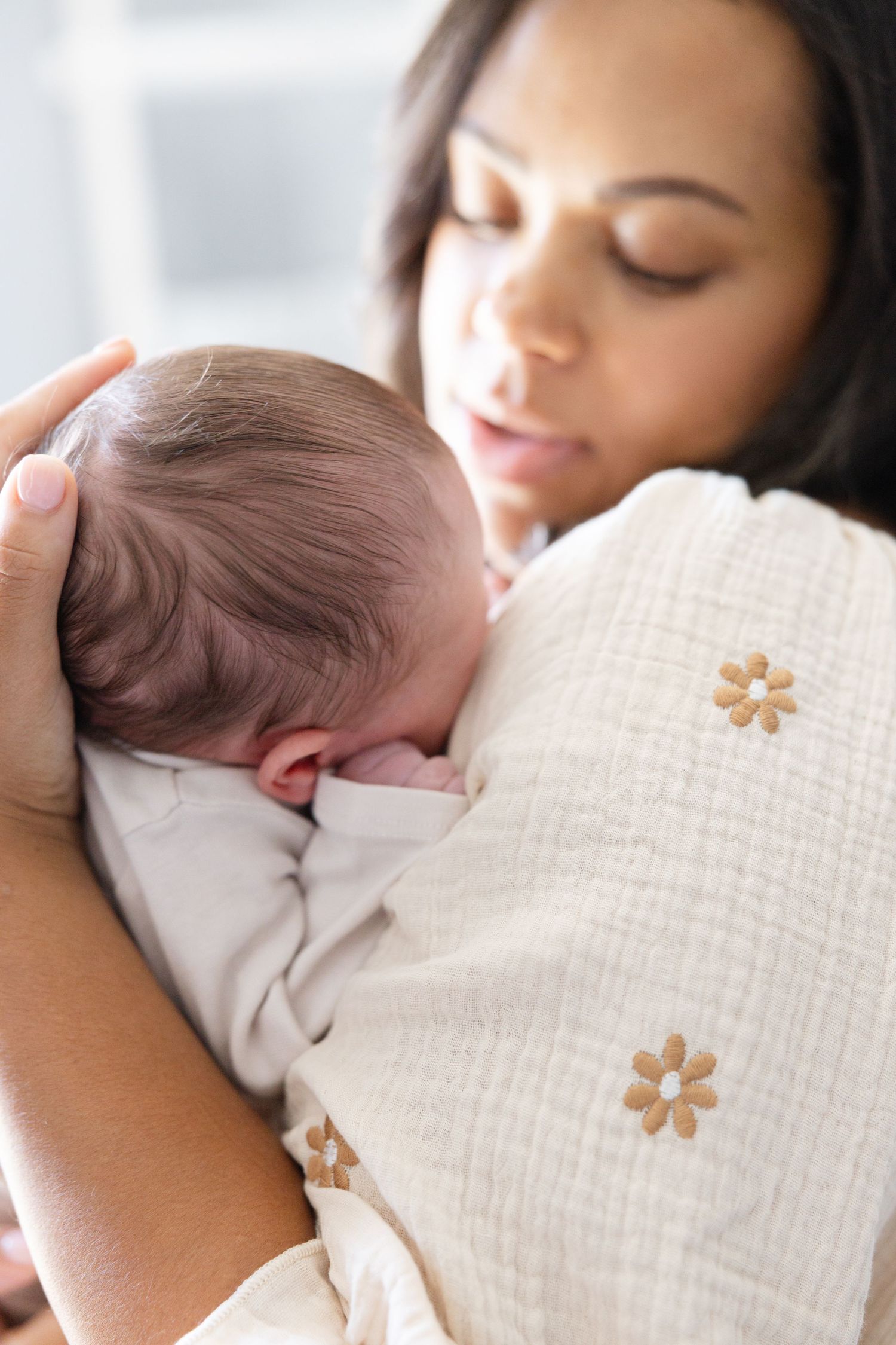 A sleeping baby rests peacefully on a white textured blanket with small floral embroidery details.