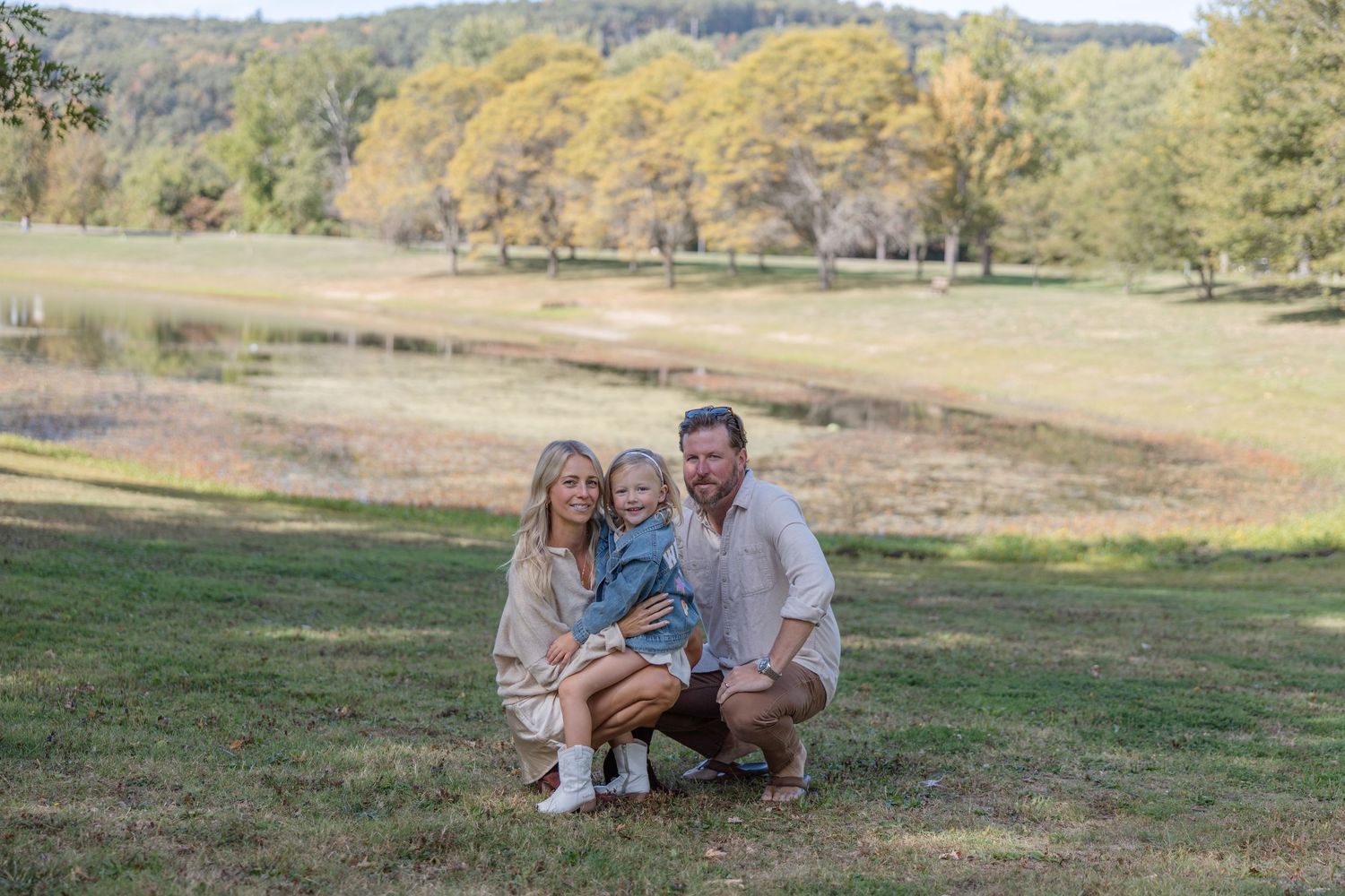 Family sitting together on grassy hill during golden hour autumn photoshoot in nature setting.
