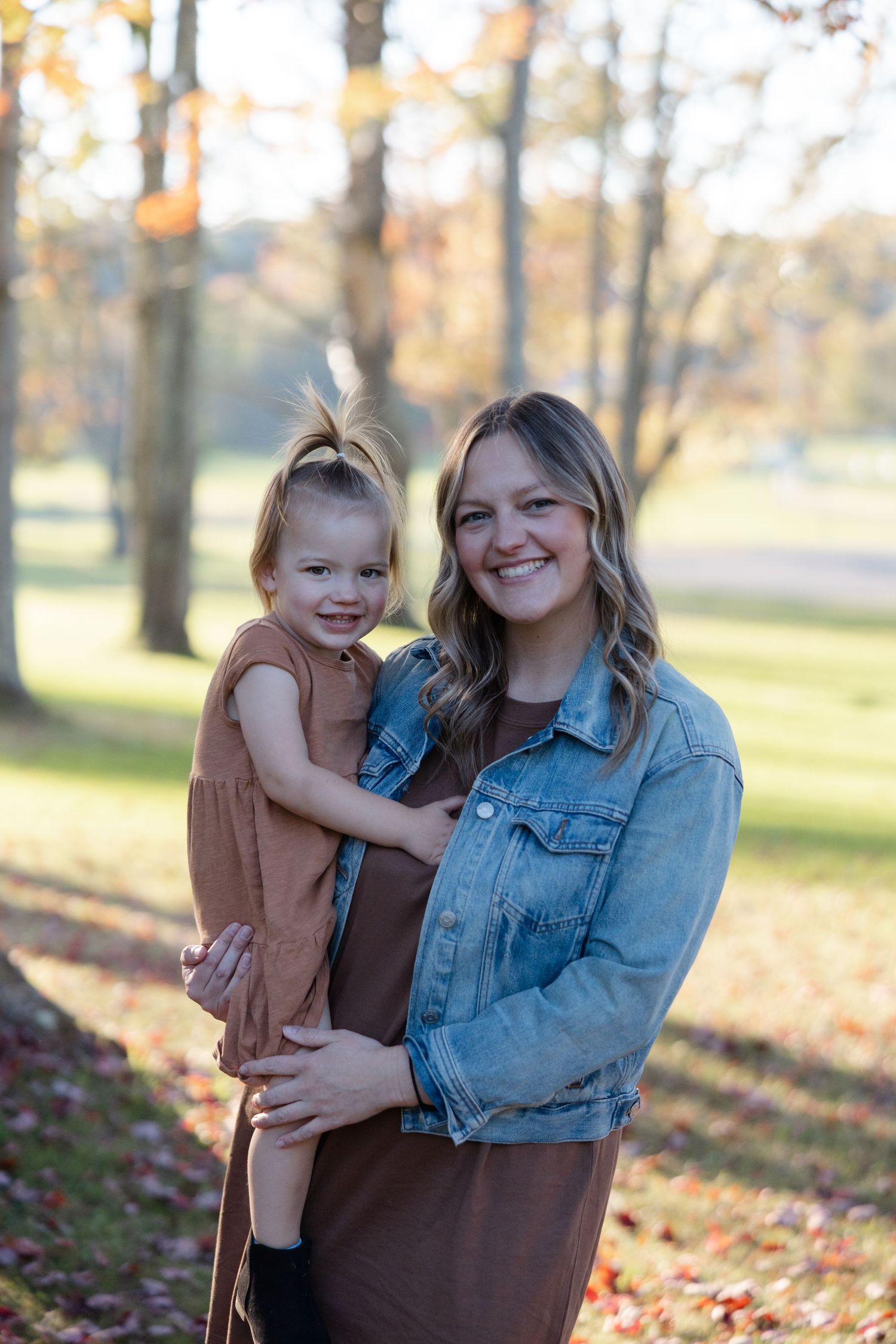 A parent and child share joyful moments together in a fall setting with autumn leaves and trees in the background.
