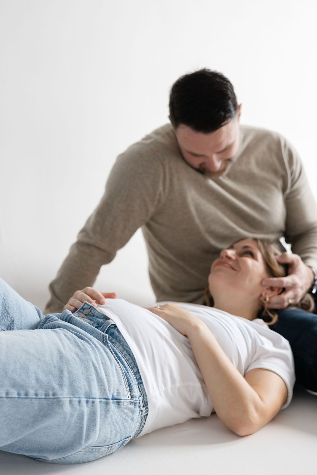 A person lying on the floor in light jeans and beige sweater shown in a sequence of four similar poses.