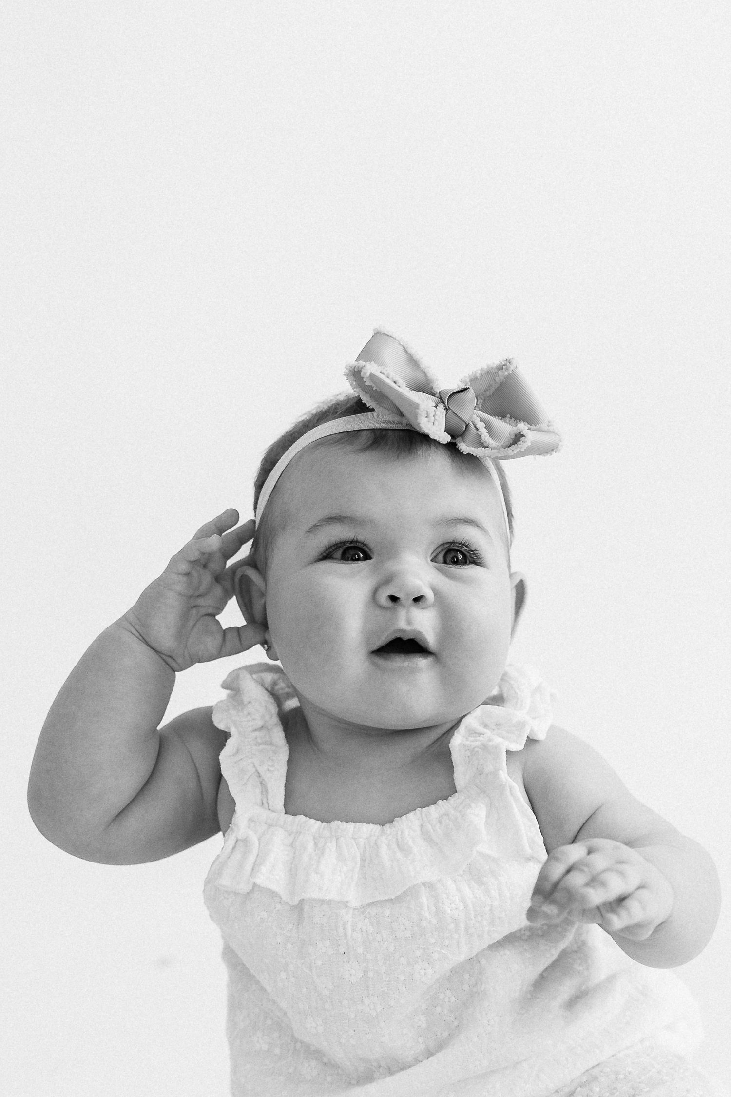 Black and white photo series of a baby in white ruffled dress making playful expressions and gestures.