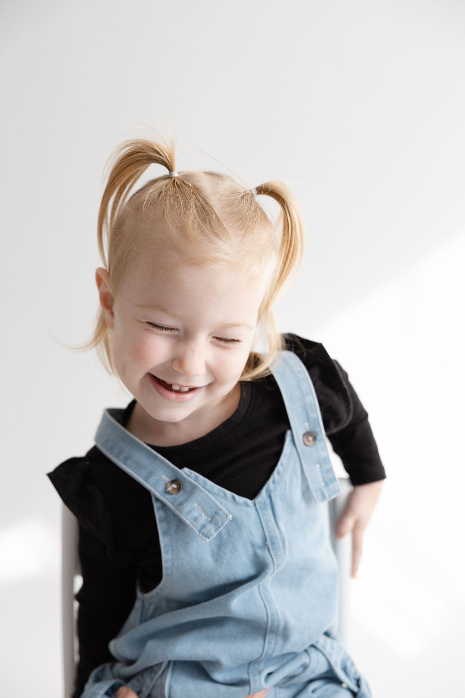 A child wearing light blue overalls and black shirt laughs joyfully in a sequence of three connected photos.