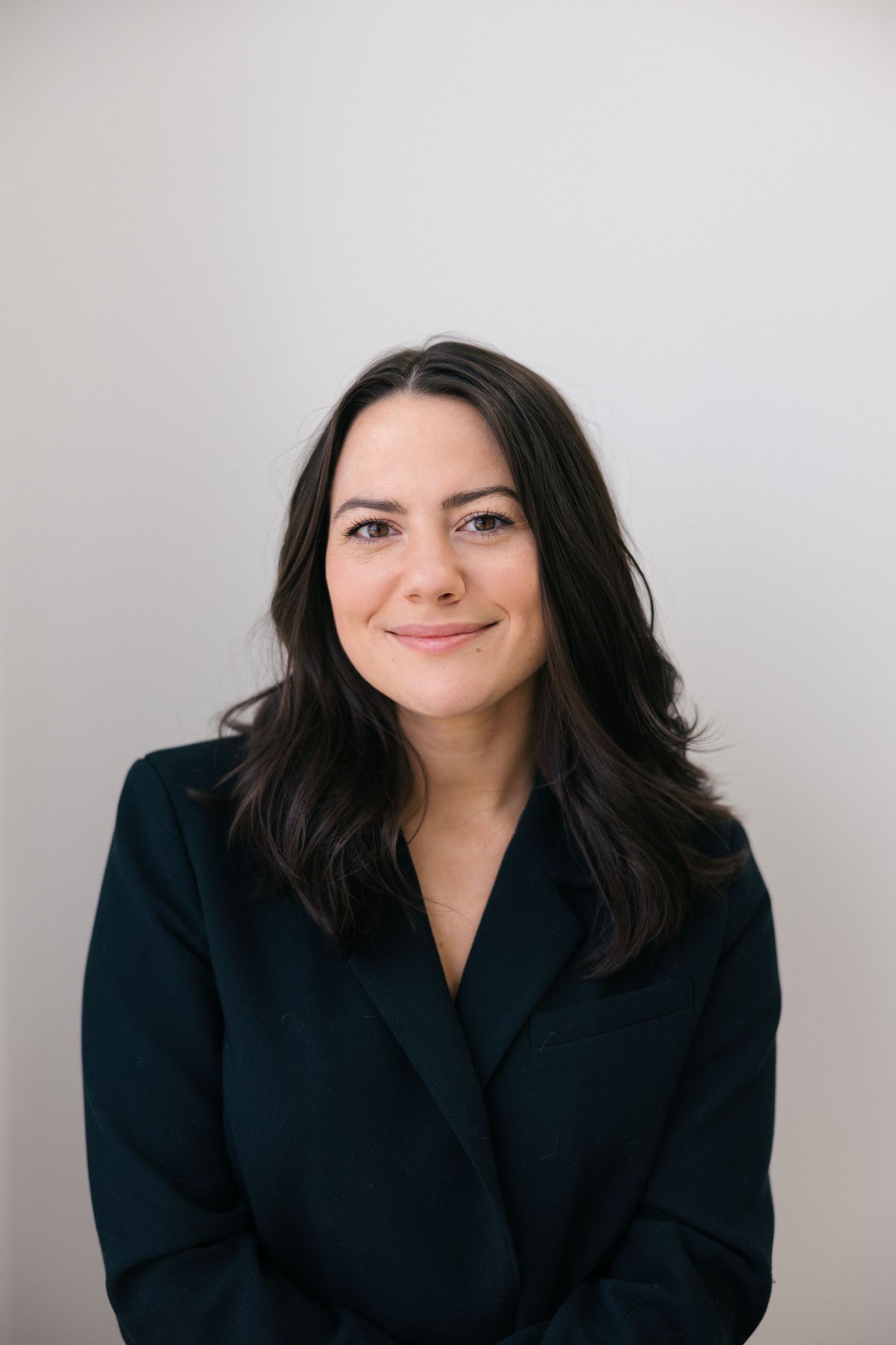 Professional headshots show person in black blazer against light background with warm smile and dark hair.