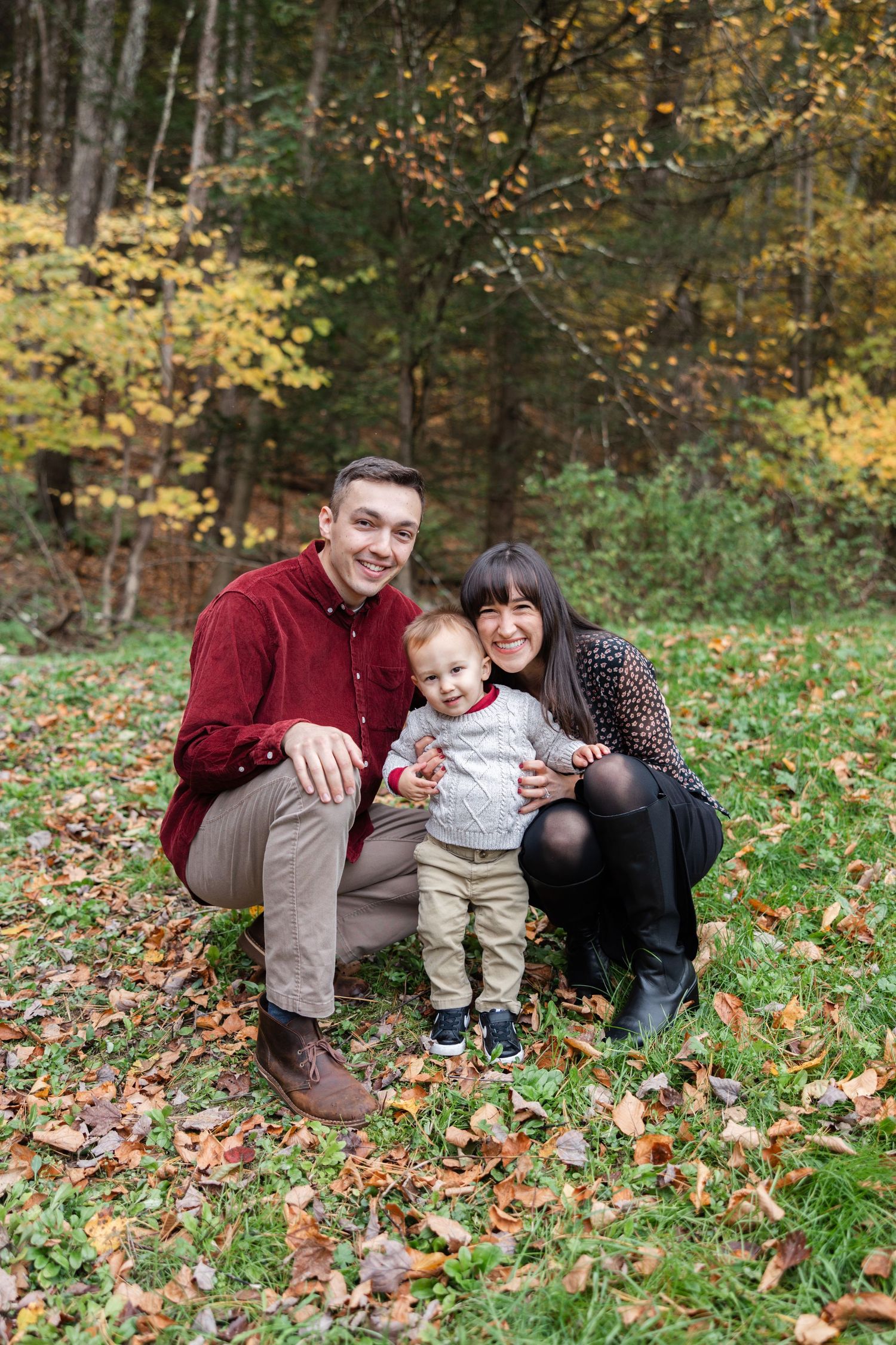 A family sits together on autumn leaves in a wooded area during a fall photo session.