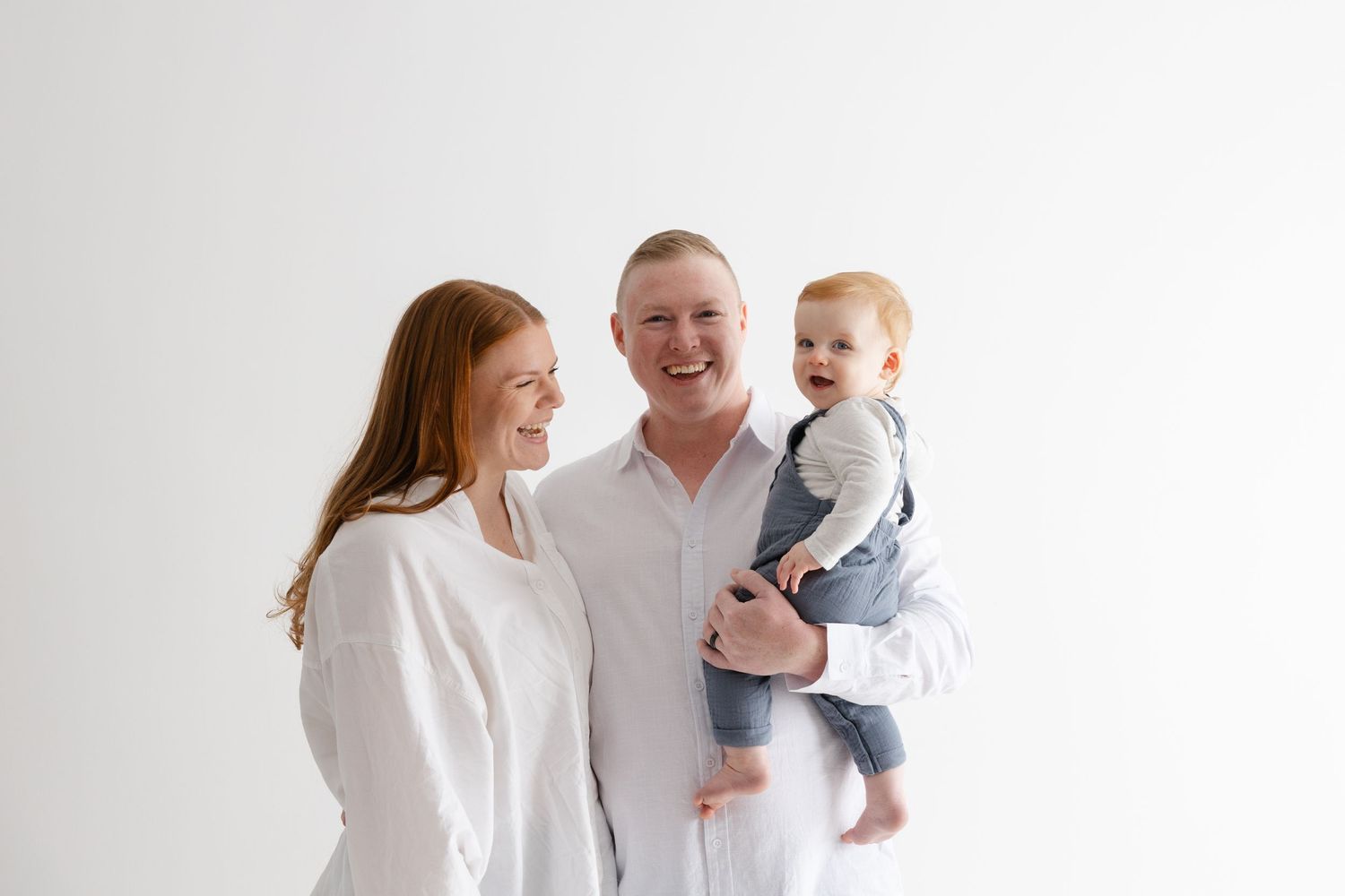 A family wearing white and gray stands together against a white background, smiling warmly.